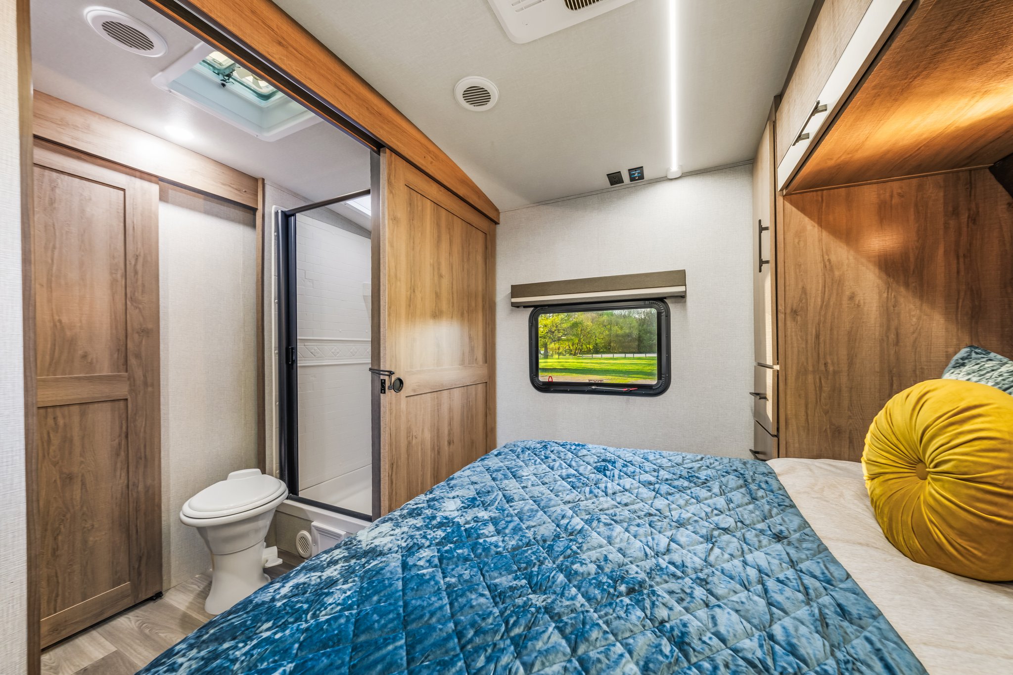 Compact RV rental bedroom with blue comforter, built-in storage, and en-suite bathroom.. Grand Design Imagine 2024