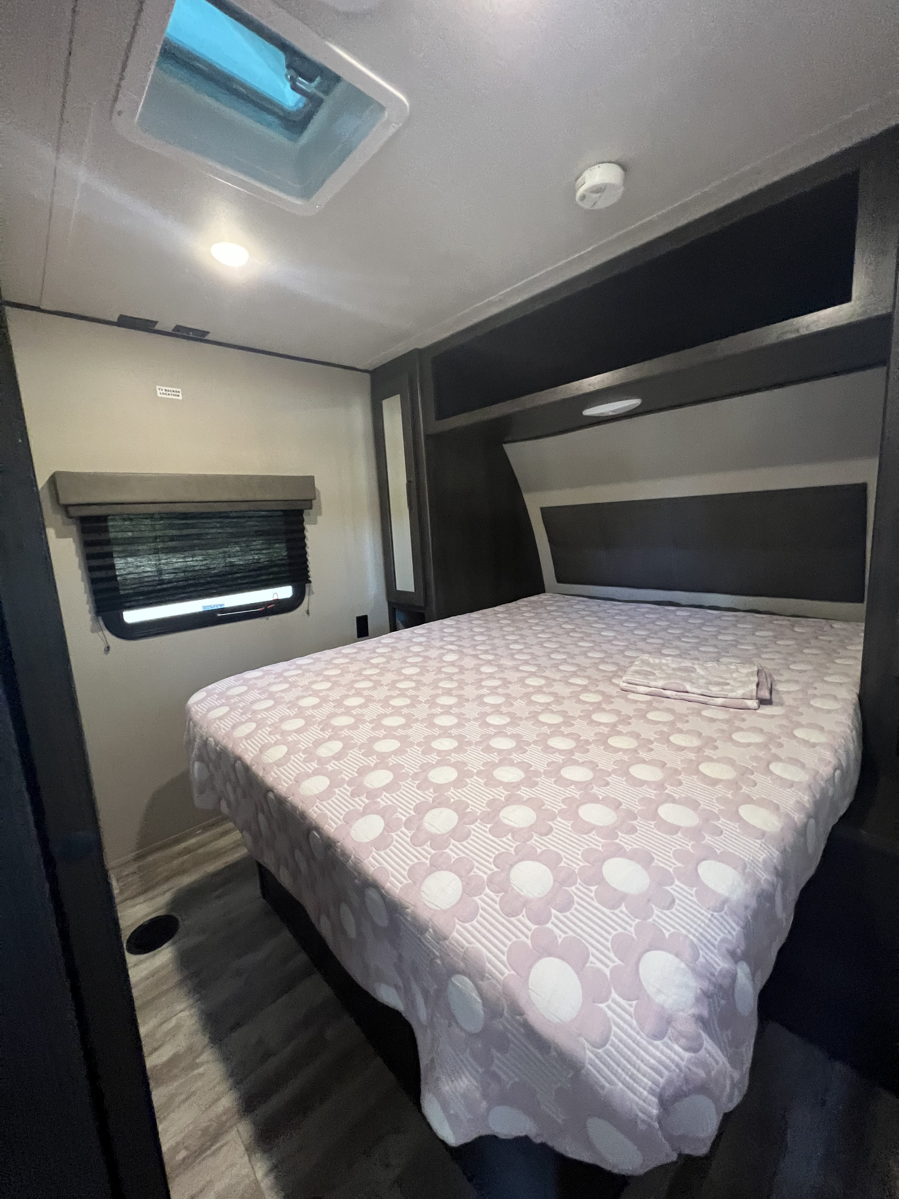 Experience comfort in this RV rental bedroom: floral bedspread, ceiling vent, & window. Features incl. smoke detector & TV mount spot.. Grand Design Transcend Xplor 2020
