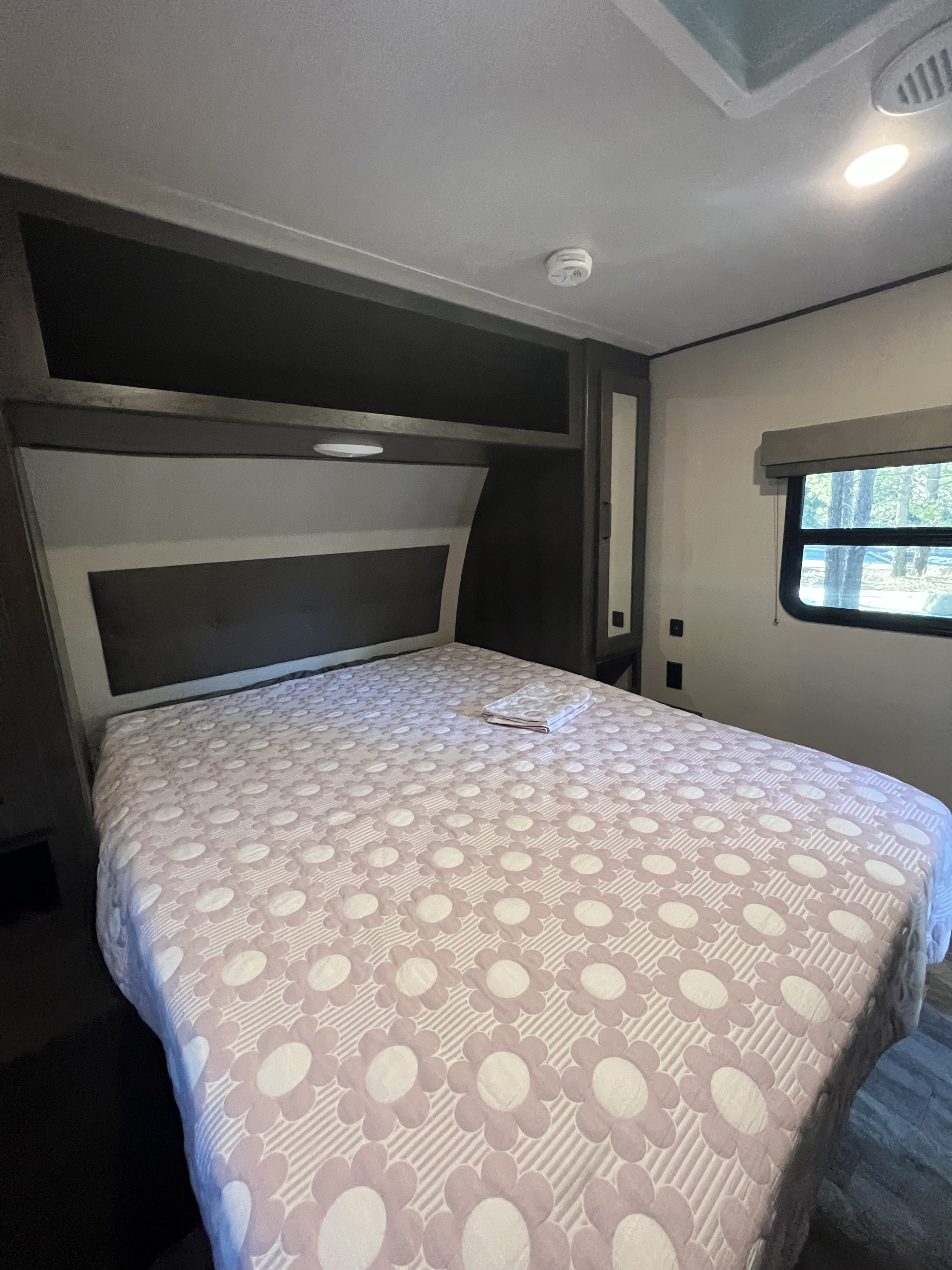 Comfortable RV rental bedroom featuring a large bed with a pink floral comforter, built-in storage, and window views.. Grand Design Transcend Xplor 2020