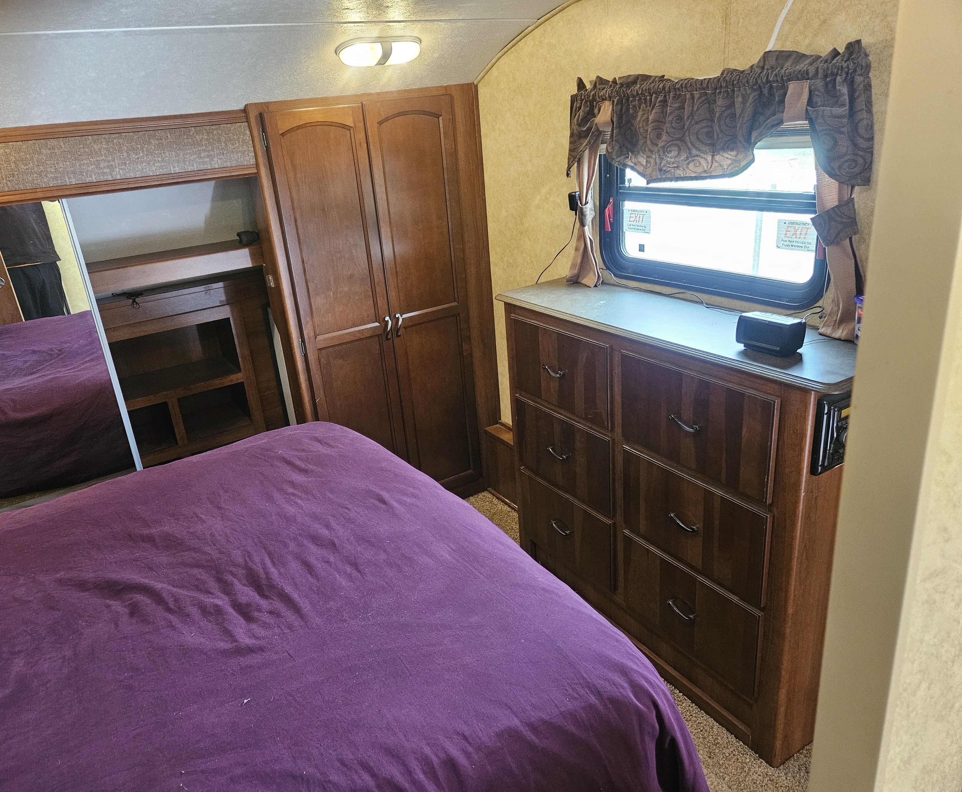 RV rental bedroom with purple bed, wood cabinets, dresser, and a window, offering comfort for your trip.. Crusader Crusader Fifth Wheel 2012