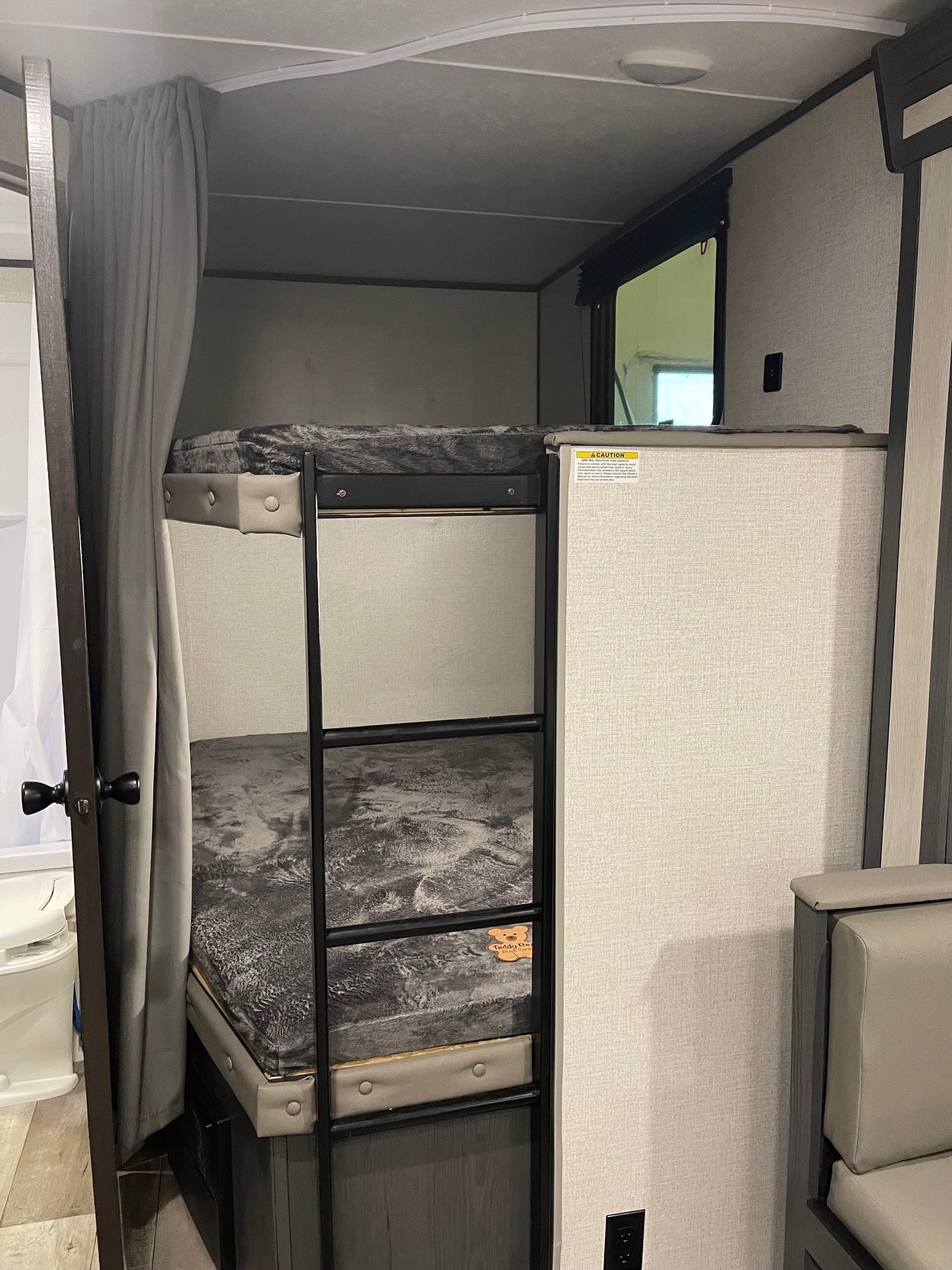 RV rental interior features compact bunk beds with grey bedding, a privacy curtain, and a window for comfortable travel.. Aspen Trail Aspen Trail Trailer 2022