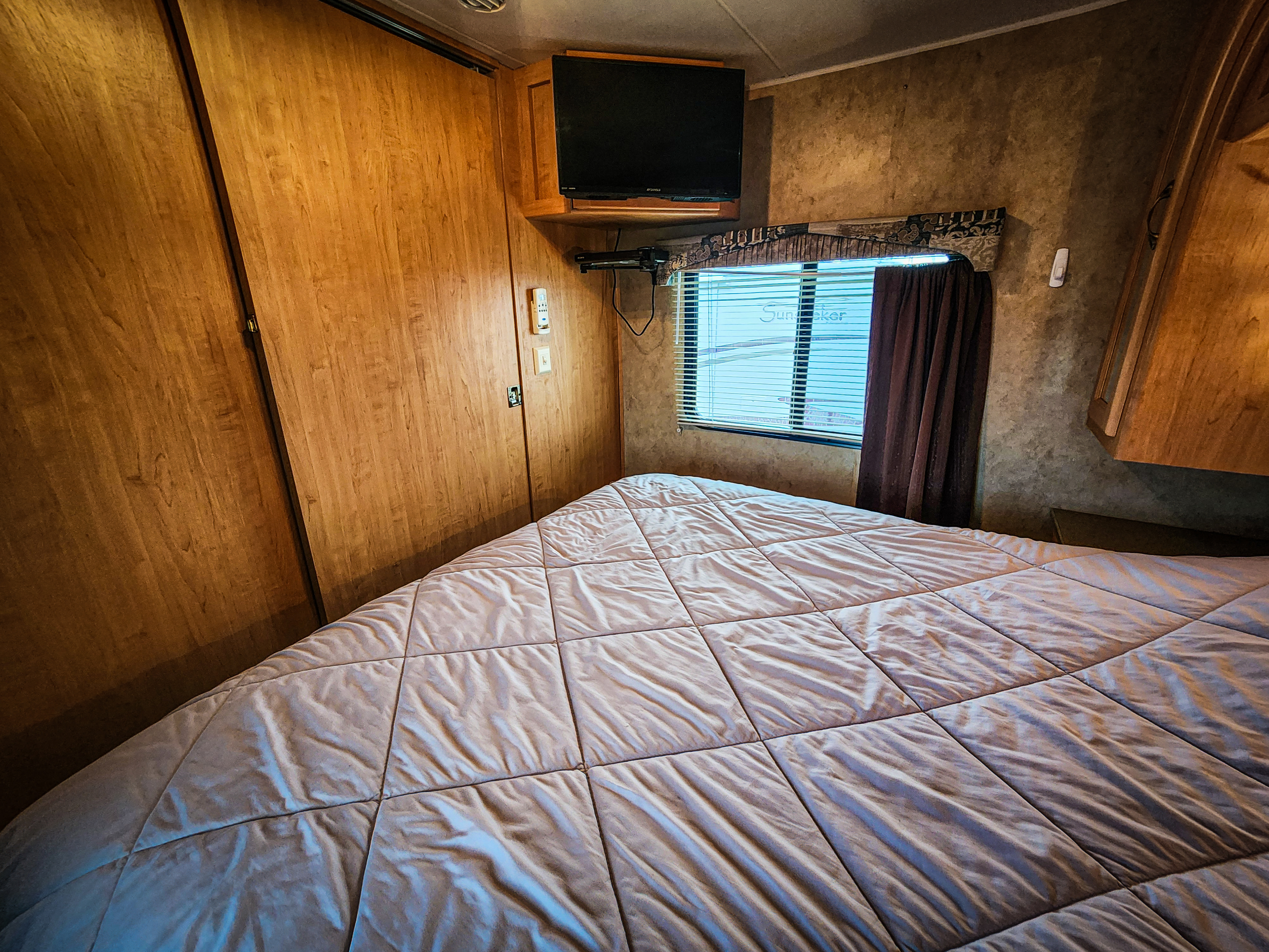 Cozy RV rental bedroom with a large quilted bed, mounted TV, and window. Perfect for travelers.. Damon Corporation Daybreak 2007