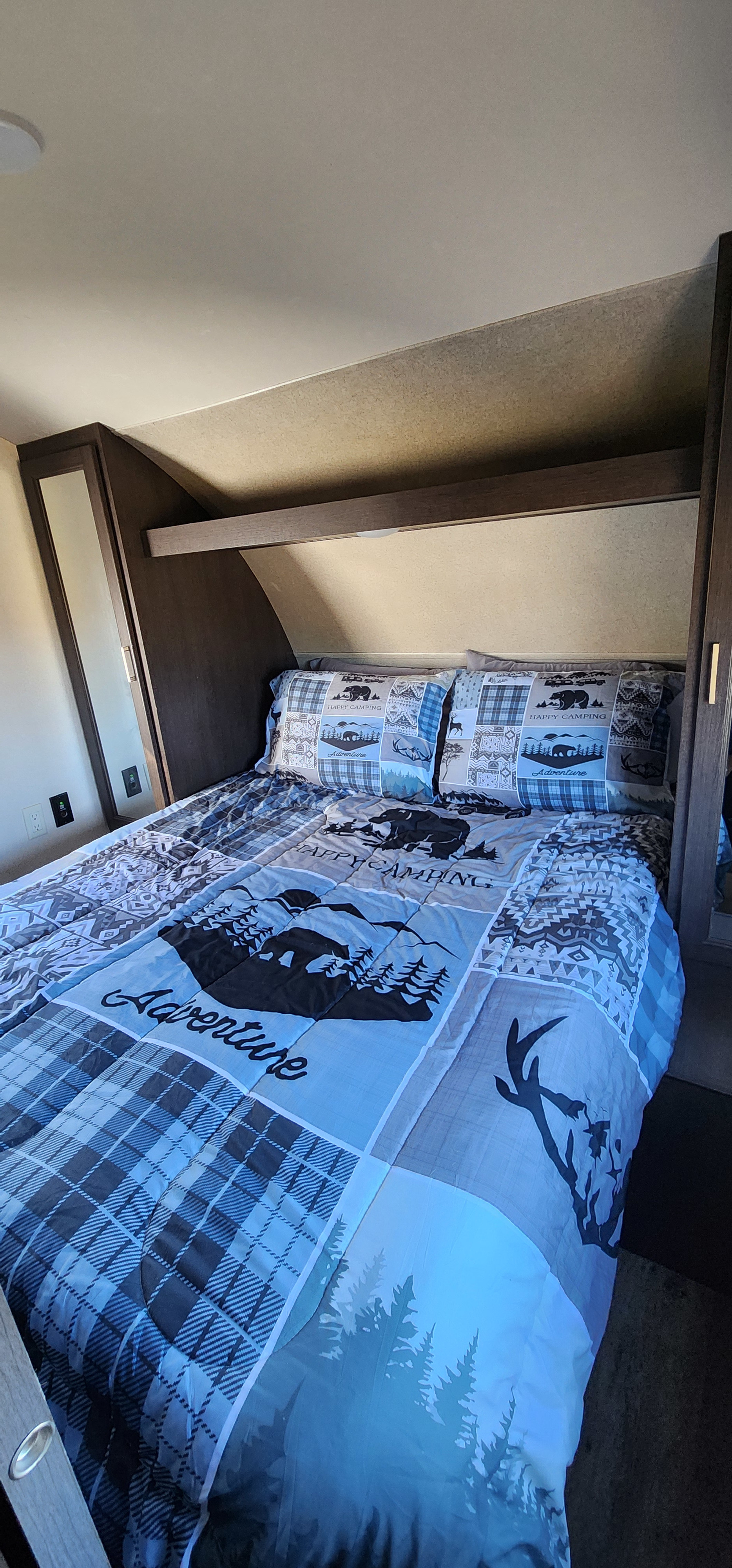 Cozy RV rental bedroom features "Happy Camping" themed bedding, built-in storage, and overhead lighting.. Forest River Wildwood X-Lite 2019