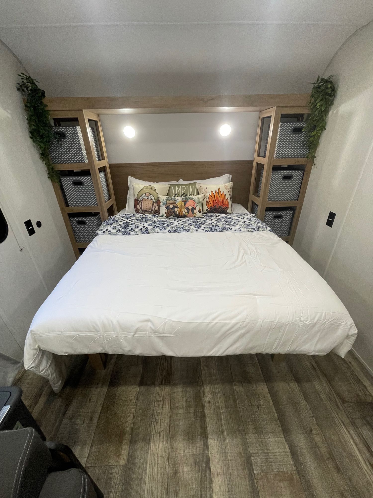 Cozy RV rental bedroom featuring a white bed, decorative pillows, built-in storage with chevron bins, and rustic wood flooring.. Forest River Cherokee Wolf Den 26EV 2024