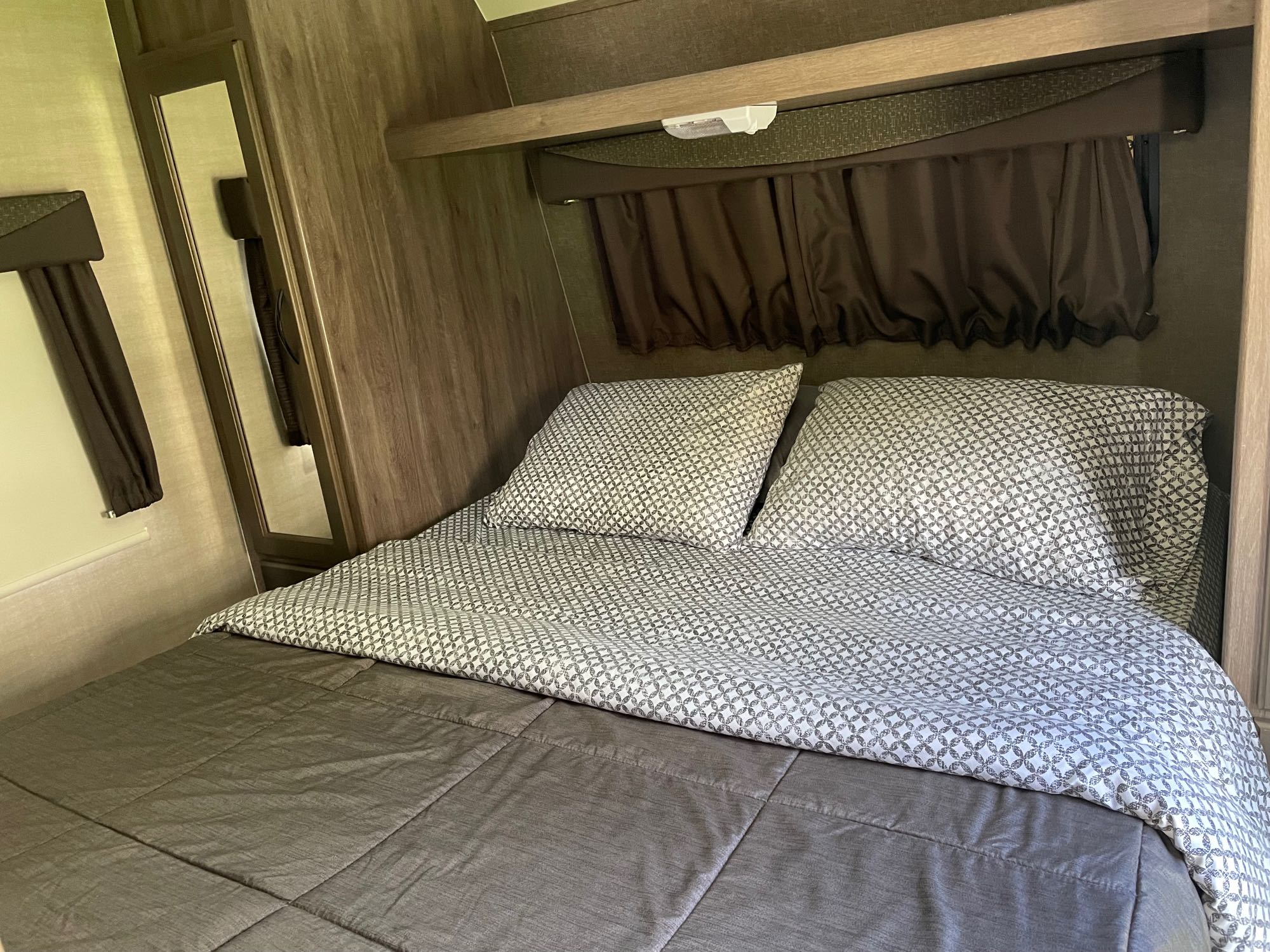 Comfortable RV rental bedroom: patterned bed, dark curtains, wooden walls, and a side mirror. Ready for your adventure.. Pacific Coachworks Surf Side Xtralite 2017