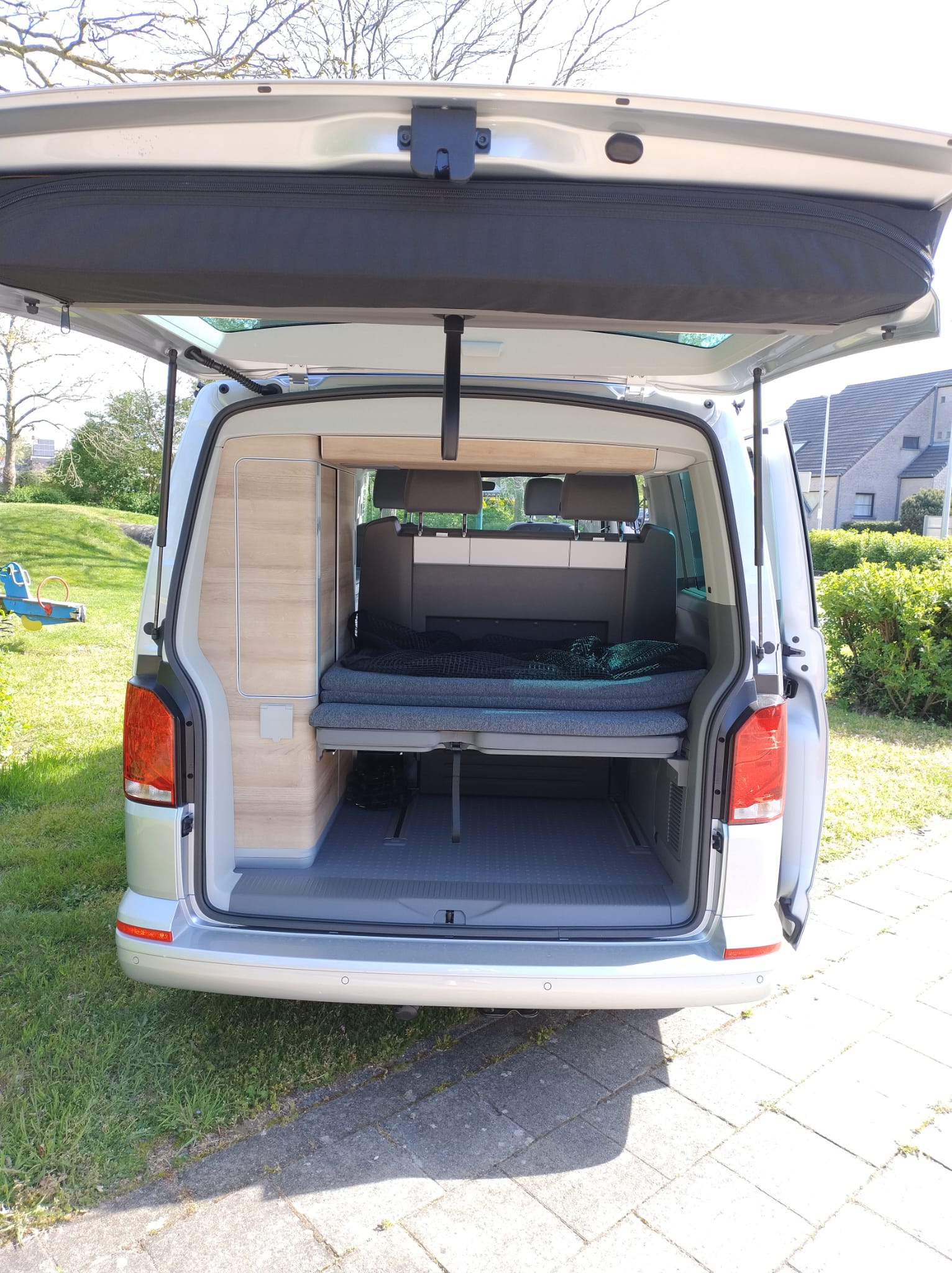 This RV rental showcases a compact camper van interior with a convertible bed, custom storage, and open tailgate.. Volkswagen California Coast T6 2024