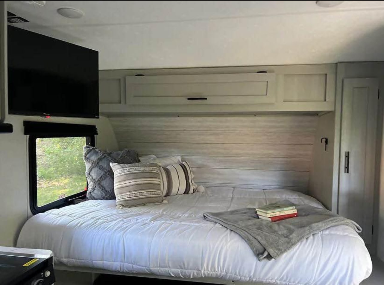 Cozy RV rental bedroom featuring a bed, mounted TV, window view, and overhead storage, perfect for travel.. Forest River Wildwood FSX Plantium 2022