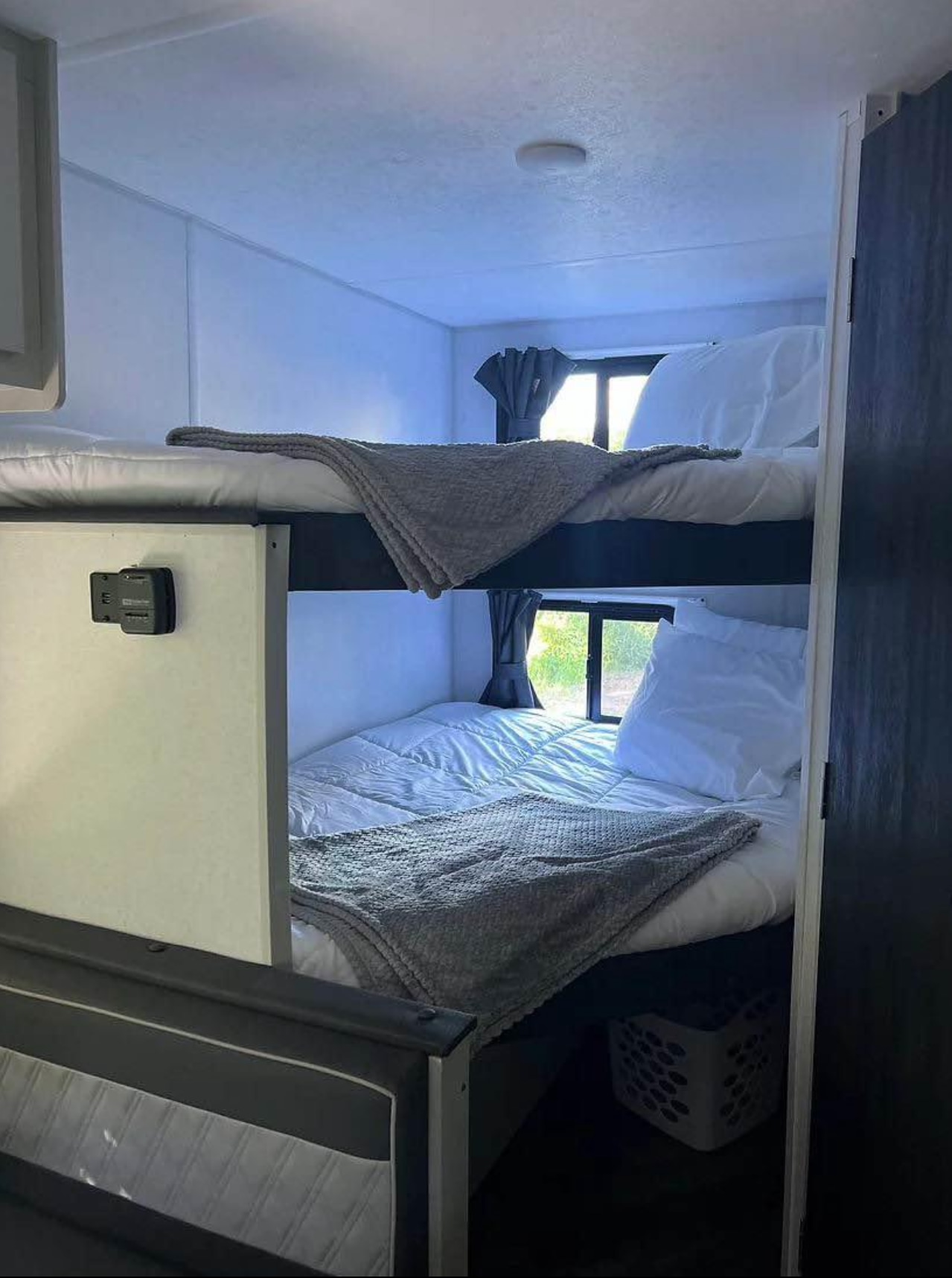 Comfy RV rental interior with bunk beds, white bedding, and grey throws. Windows show green outside, perfect for travel.. Forest River Wildwood FSX Plantium 2022