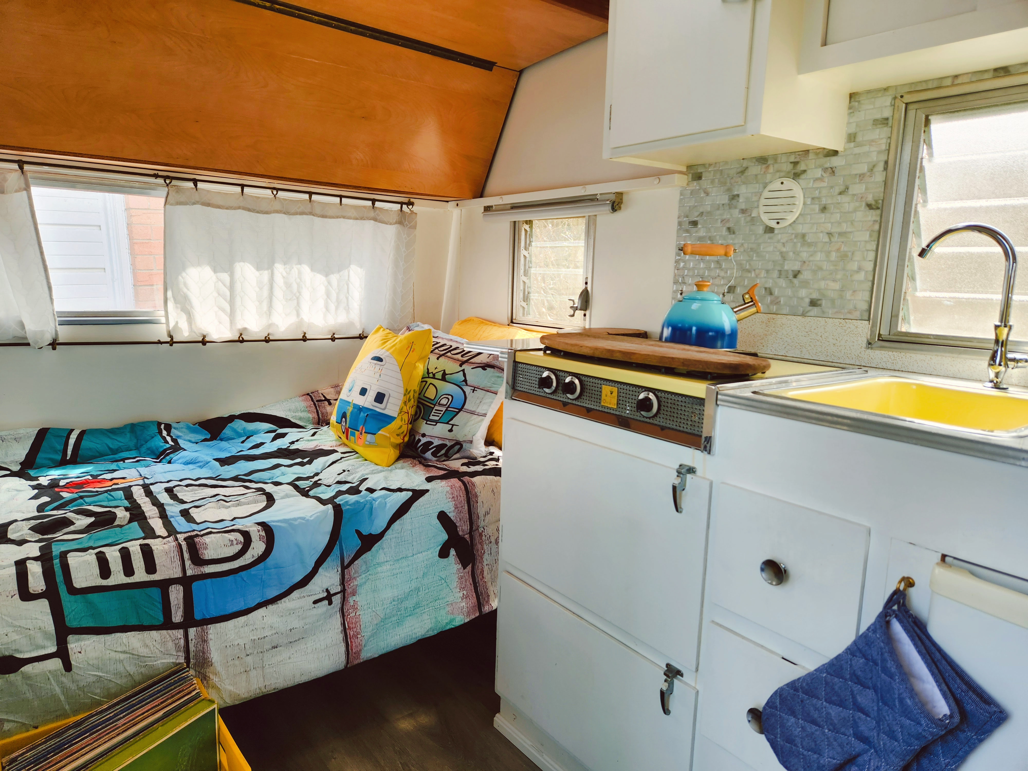 Cozy rv rental interior showcasing a bright bed with pillows, functional kitchen with a yellow sink, and wood ceilings.. Vintage Trailers pyramid 1959