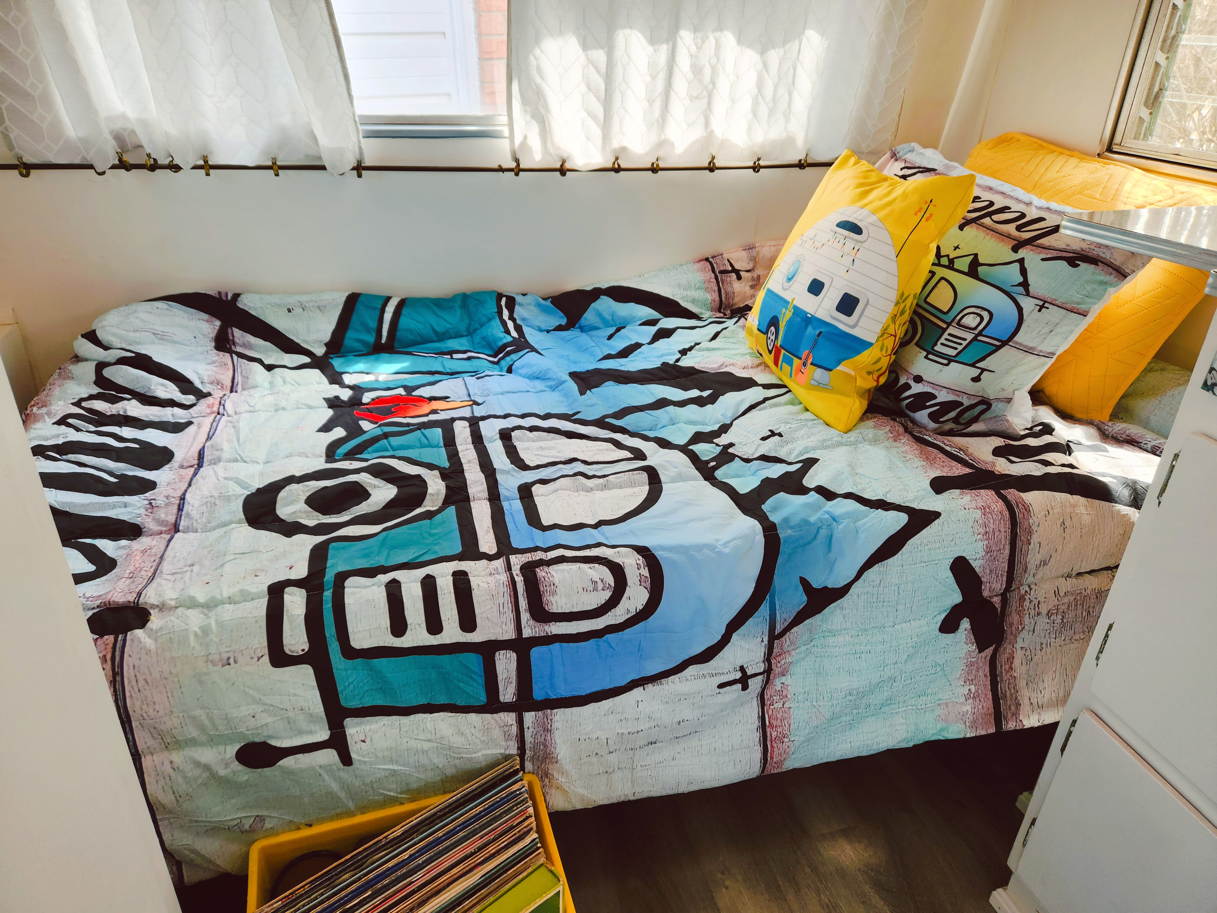 Inside a comfortable RV rental, featuring a vibrant bed with unique patterns, camper-themed pillows, and bright windows.. Vintage Trailers pyramid 1959