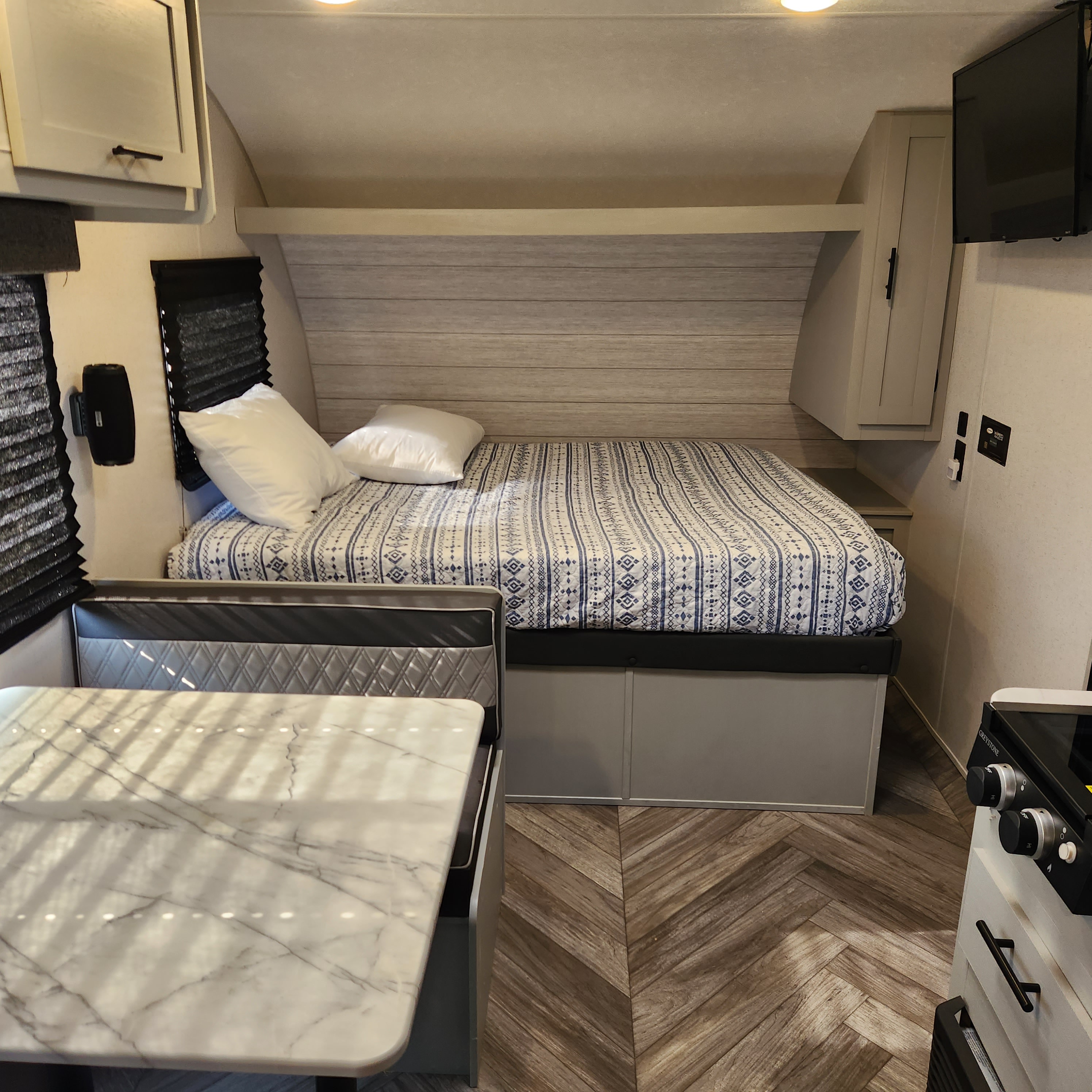 Modern RV rental interior with a comfy bed, dinette, overhead storage, and light wood chevron flooring.. Forest River Wildwood FSX Plantium 2022