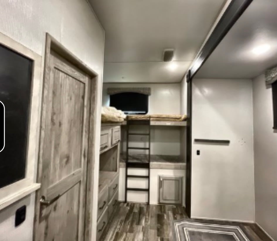 RV rental bunkhouse interior with modern light wood bunks, ladder, and storage. White walls & wood-grain floor for family trips.. Keystone RV Avalanche 2021