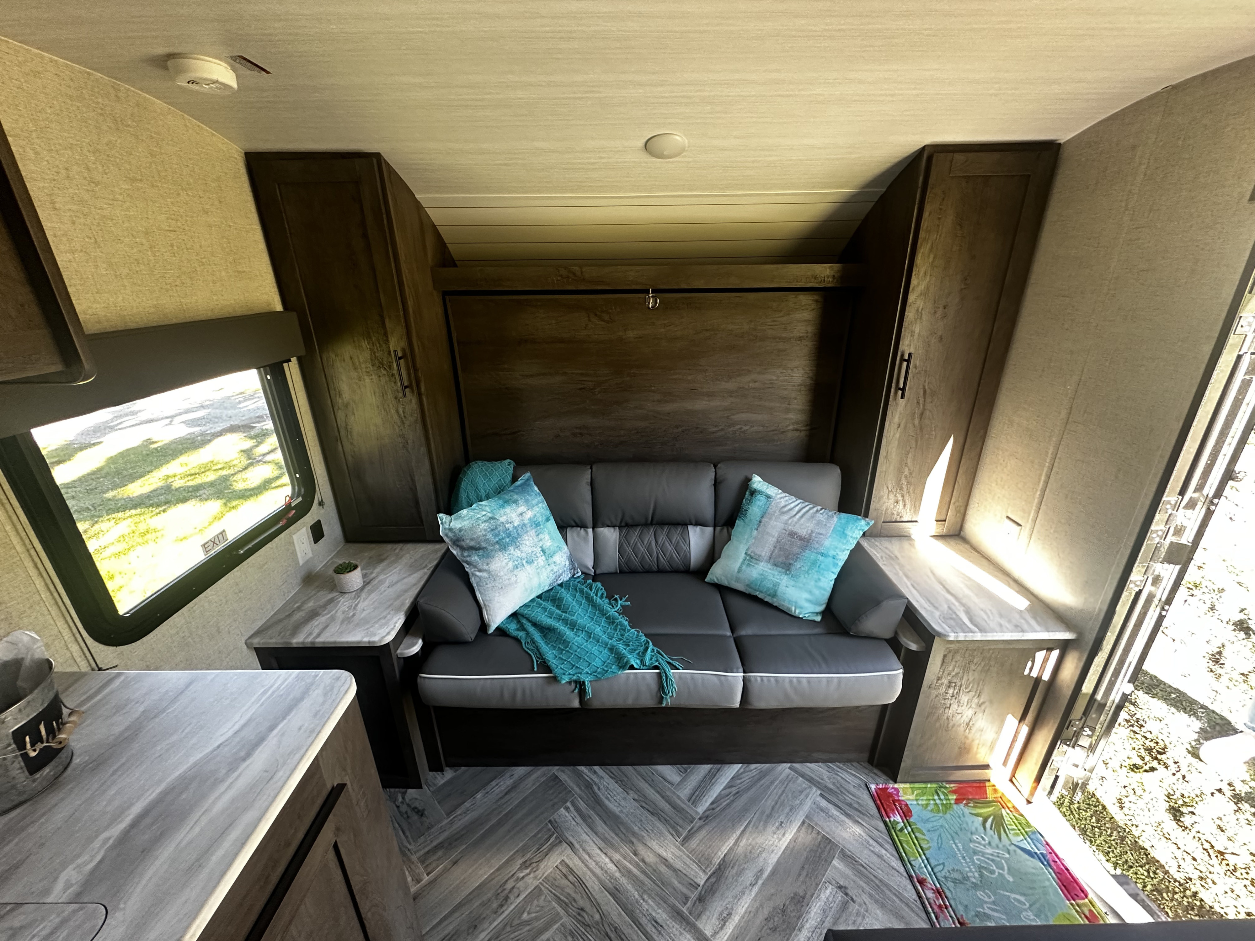 Modern RV rental interior: A comfy grey sofa with blue pillows, flanked by cabinets, on stylish herringbone flooring. Bright living space.. Forest River Salem Cruise Lite 2021