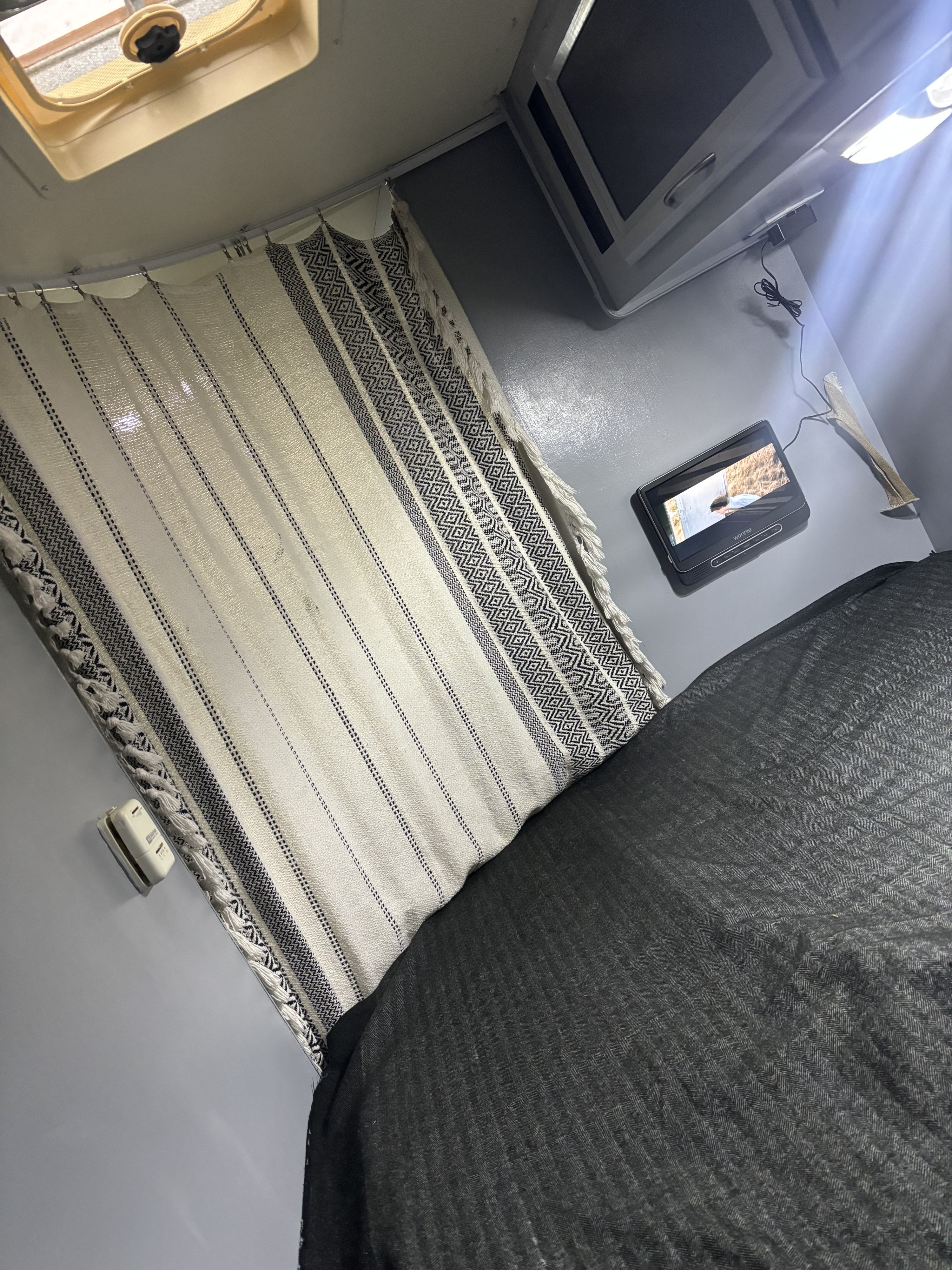 Cozy RV rental interior showing a patterned privacy curtain, portable media player, and dark herringbone bed. Overhead light and ceiling vent.. Thor Chateau 2014