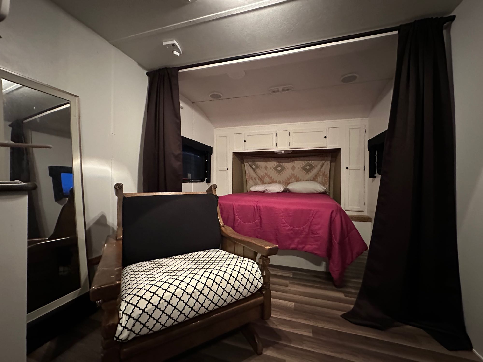 RV rental interior features a cozy bedroom with pink bed and white cabinets, plus a comfortable living area with wooden chair.. Layton Joey 2012