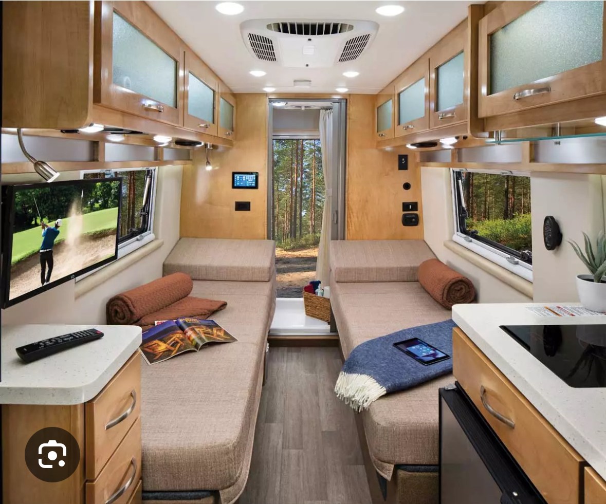 Spacious RV rental interior with dual beds, kitchenette, TV, and forest view, ideal for a cozy road trip.. Forest River Coachmen Nova 2021