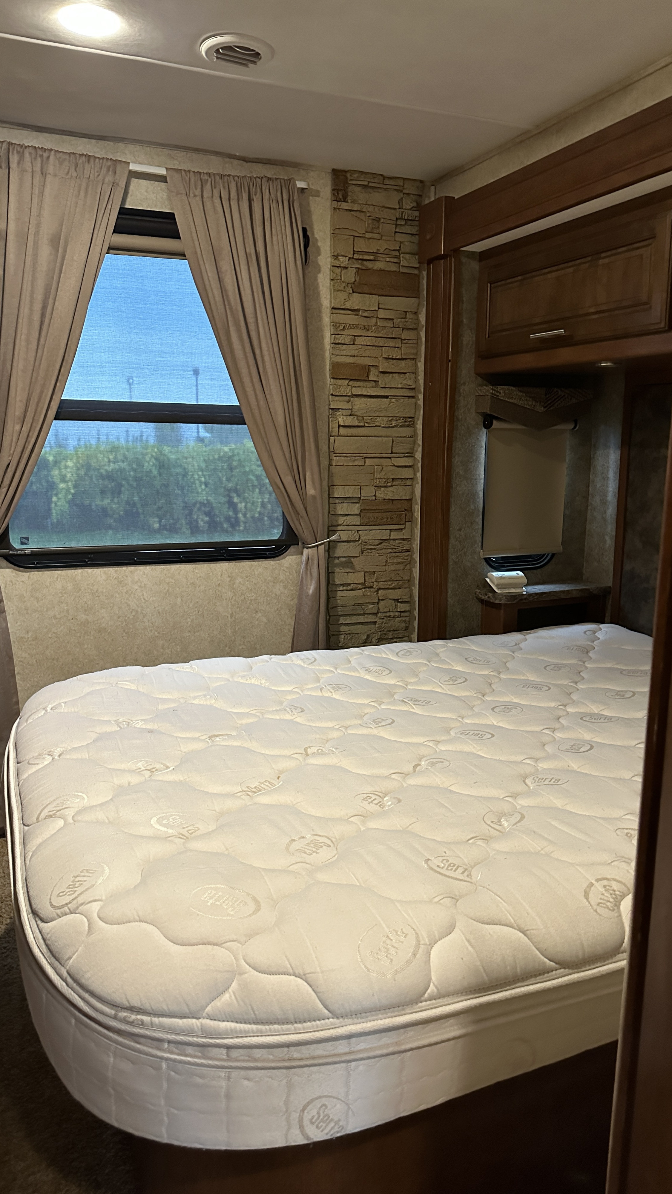 Cozy RV rental bedroom with a Serta mattress, window, stone wall, and wood cabinetry. Enjoy your travels!. Forest River Georgetown 2015