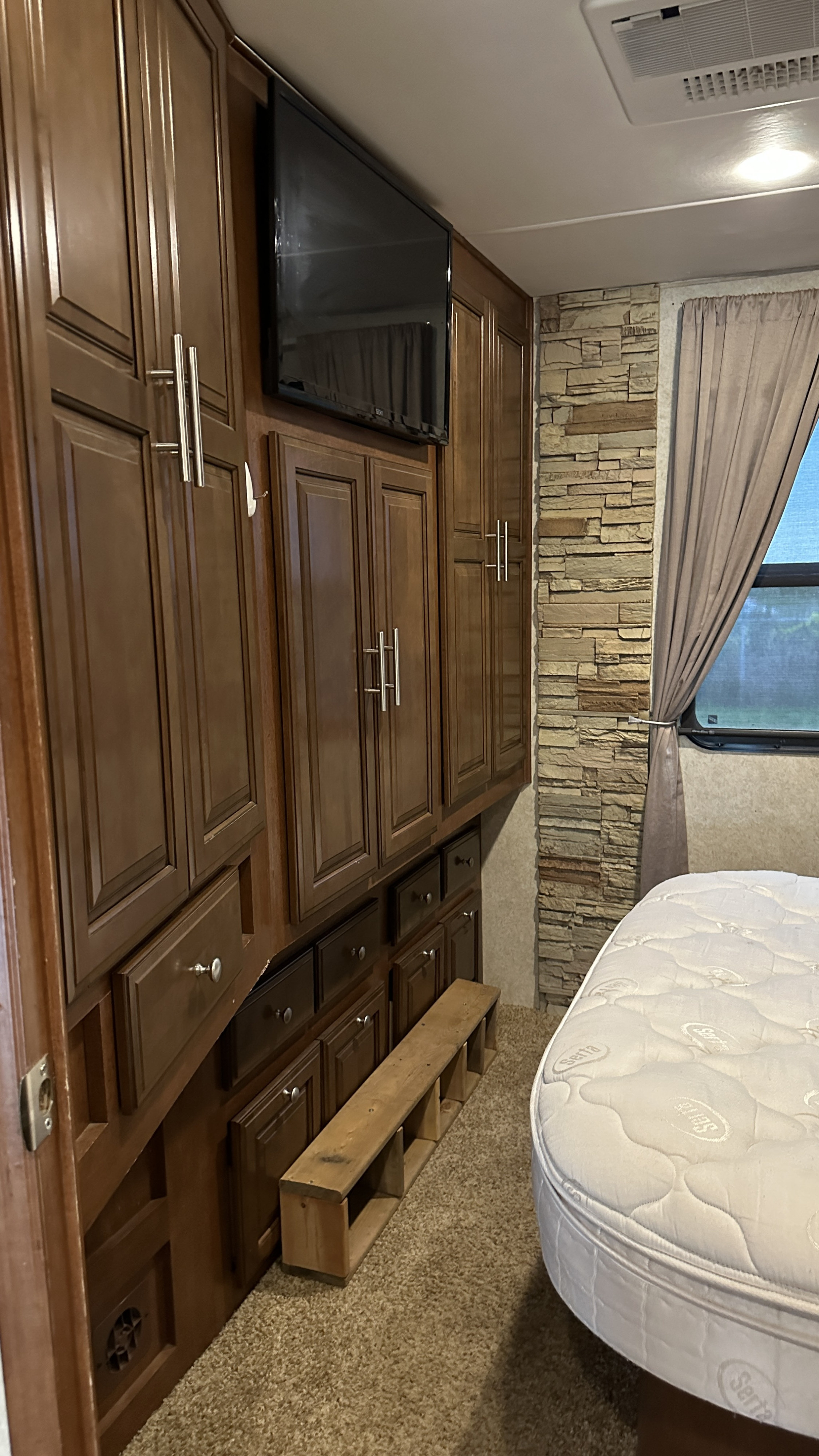 Inside an RV rental: a cozy bedroom with dark wood cabinets, TV, Serta mattress, and a stylish stone accent wall.. Forest River Georgetown 2015