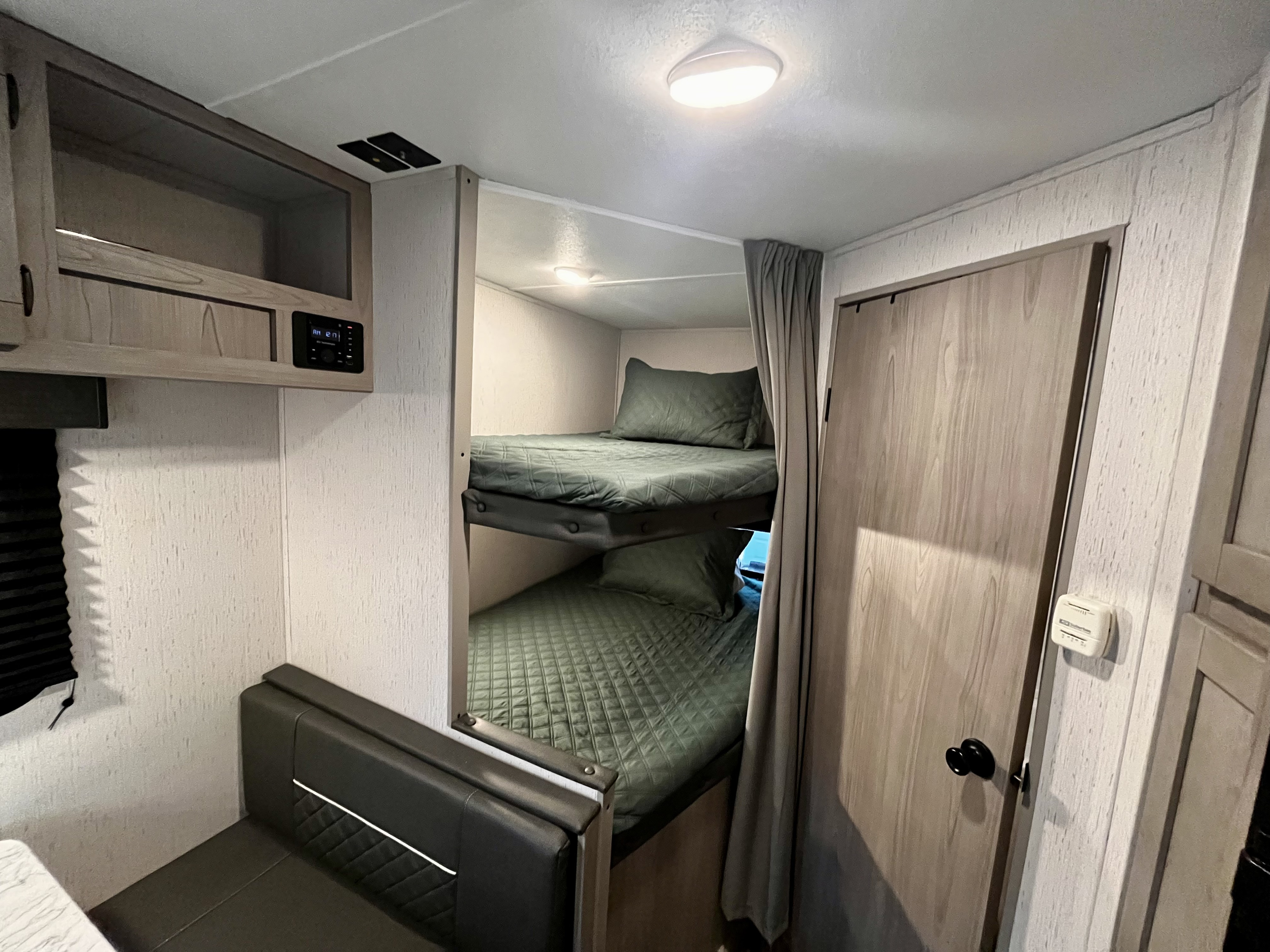 Cozy RV rental interior featuring green bunk beds, a dinette seating area, and overhead storage, designed for comfortable travel.. Dutchmen Coleman Lantern 2023