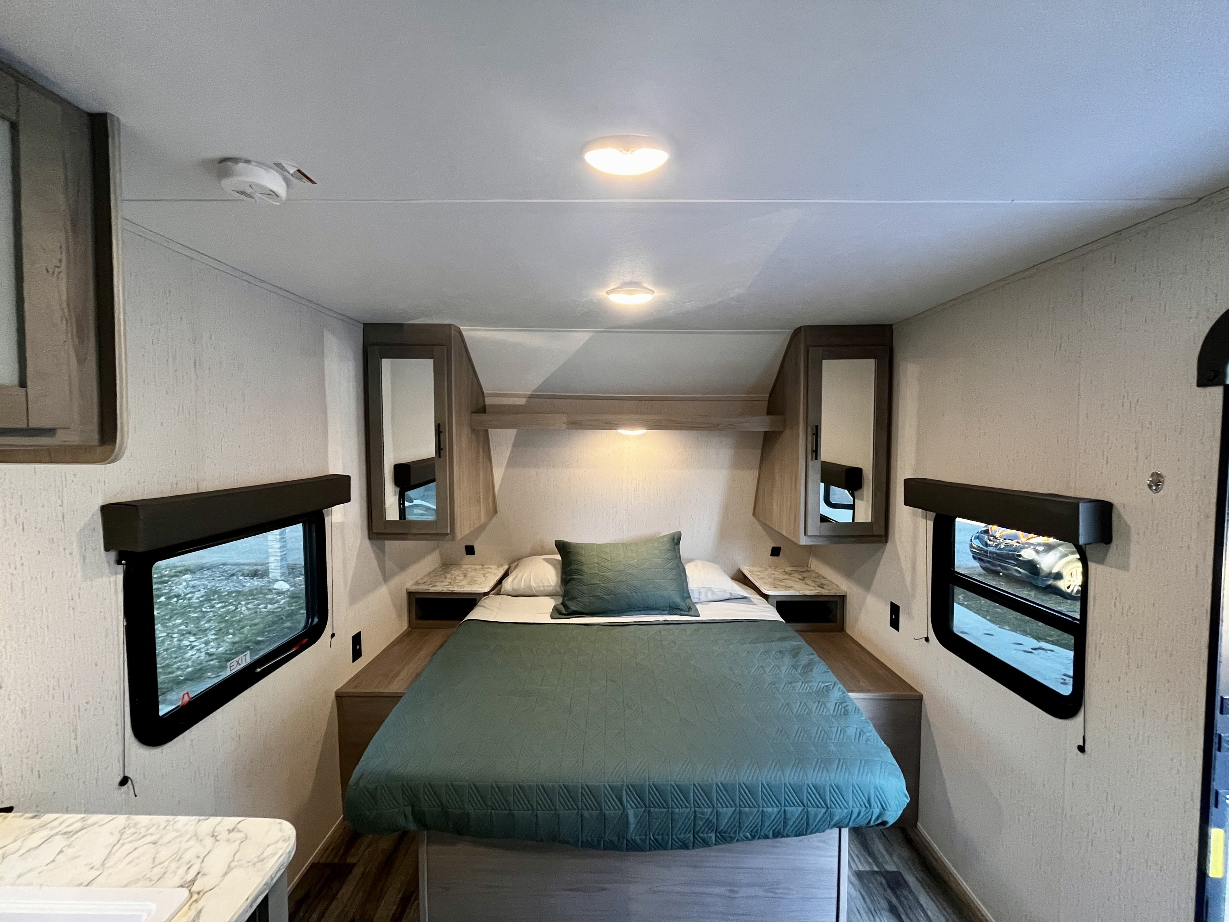 Discover comfort in this RV rental bedroom. Features a cozy bed with green bedding, overhead storage, and natural light from side windows.. Dutchmen Coleman Lantern 2023