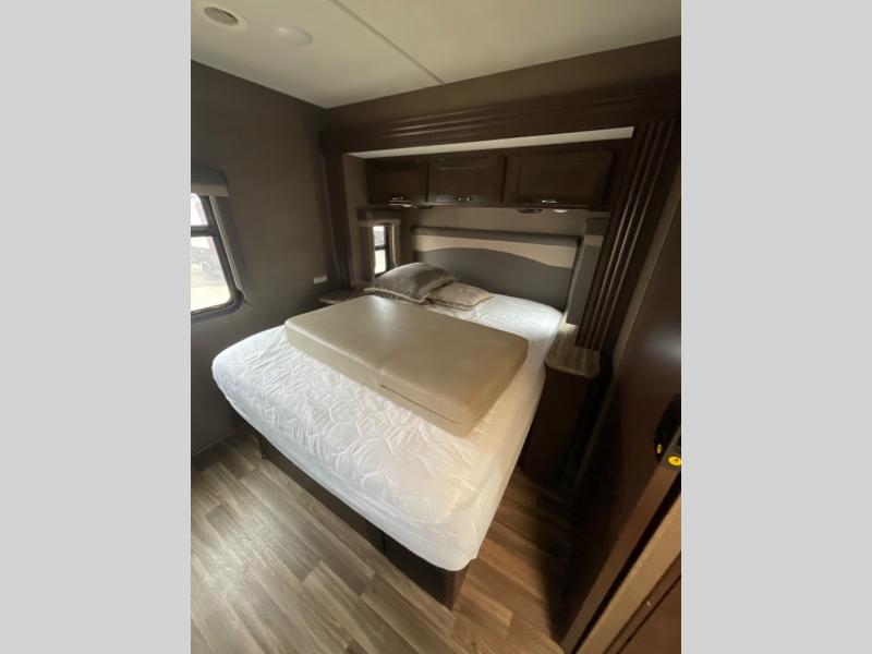 RV rental bedroom: Features a comfortable bed with a tan cushion, overhead cabinets, and a window for natural light.. Thor Motor Coach A.C.E 2018