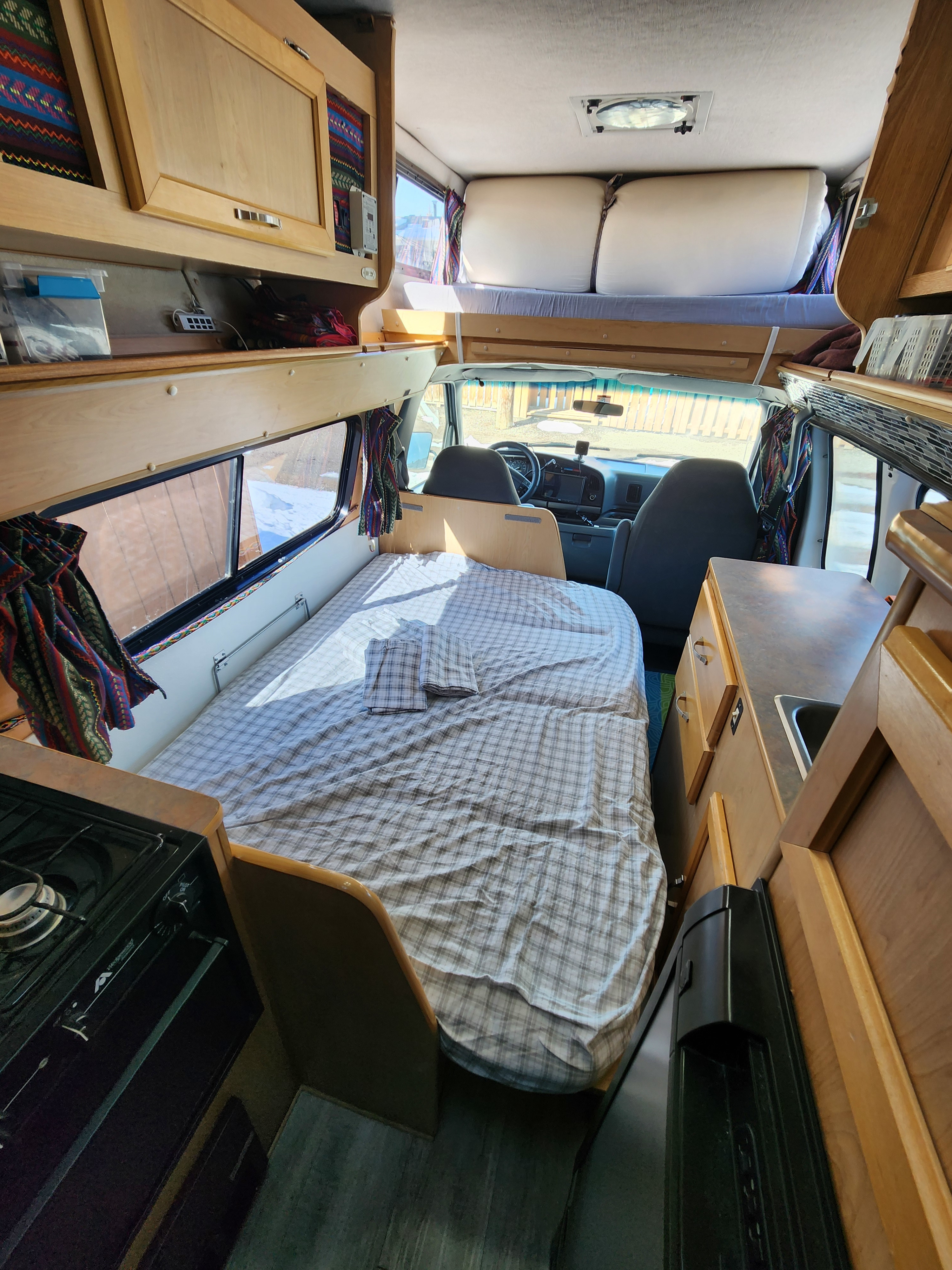 Cozy RV rental interior with a comfy bed, functional kitchen, and an elevated bunk area, perfect for mobile adventures.. Okanagan Adventure Series 1996