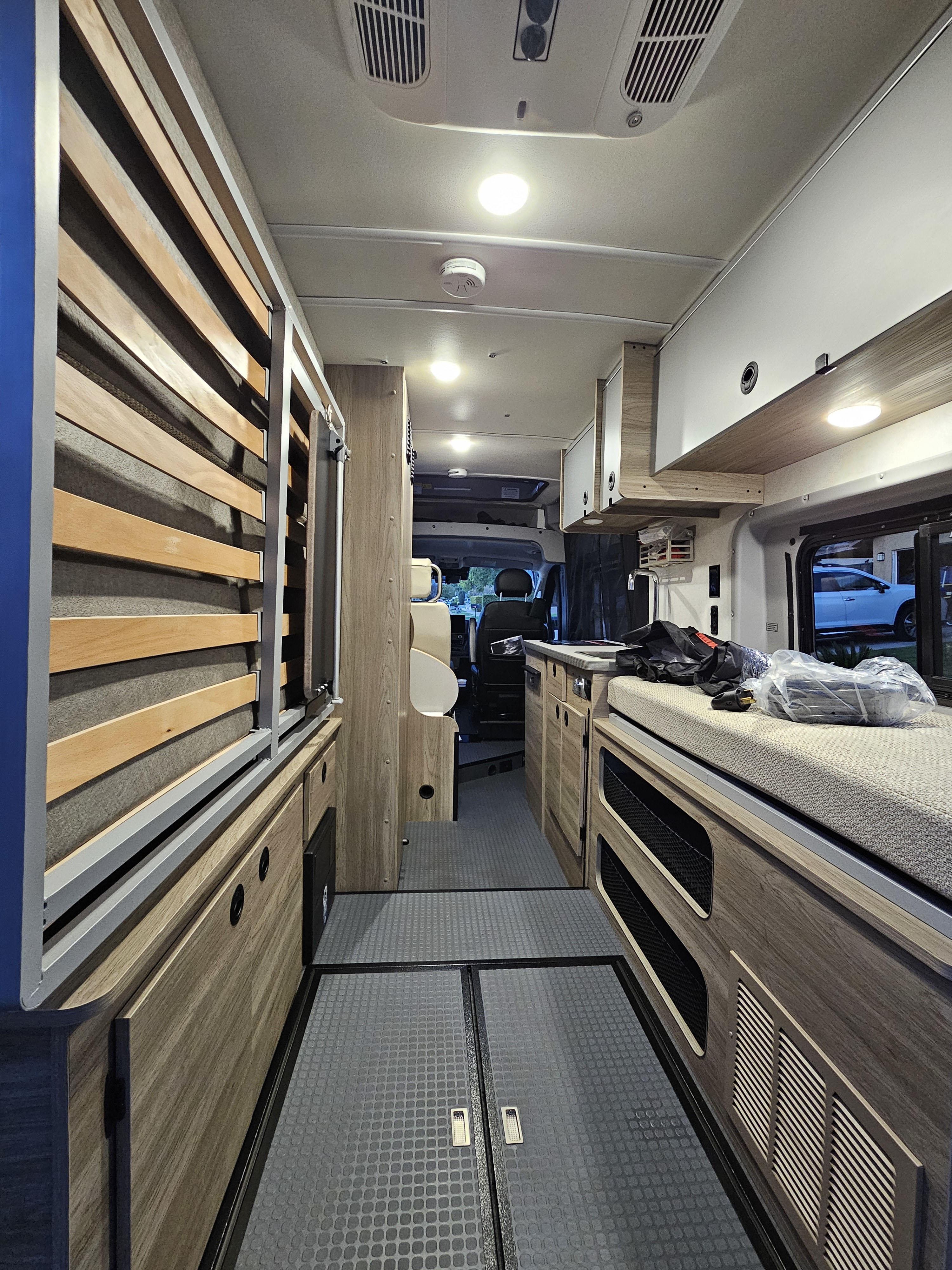 RV rental camper van interior. View of the modern wooden cabinetry, bed area, and forward cockpit.. Winnebago Solis 2023