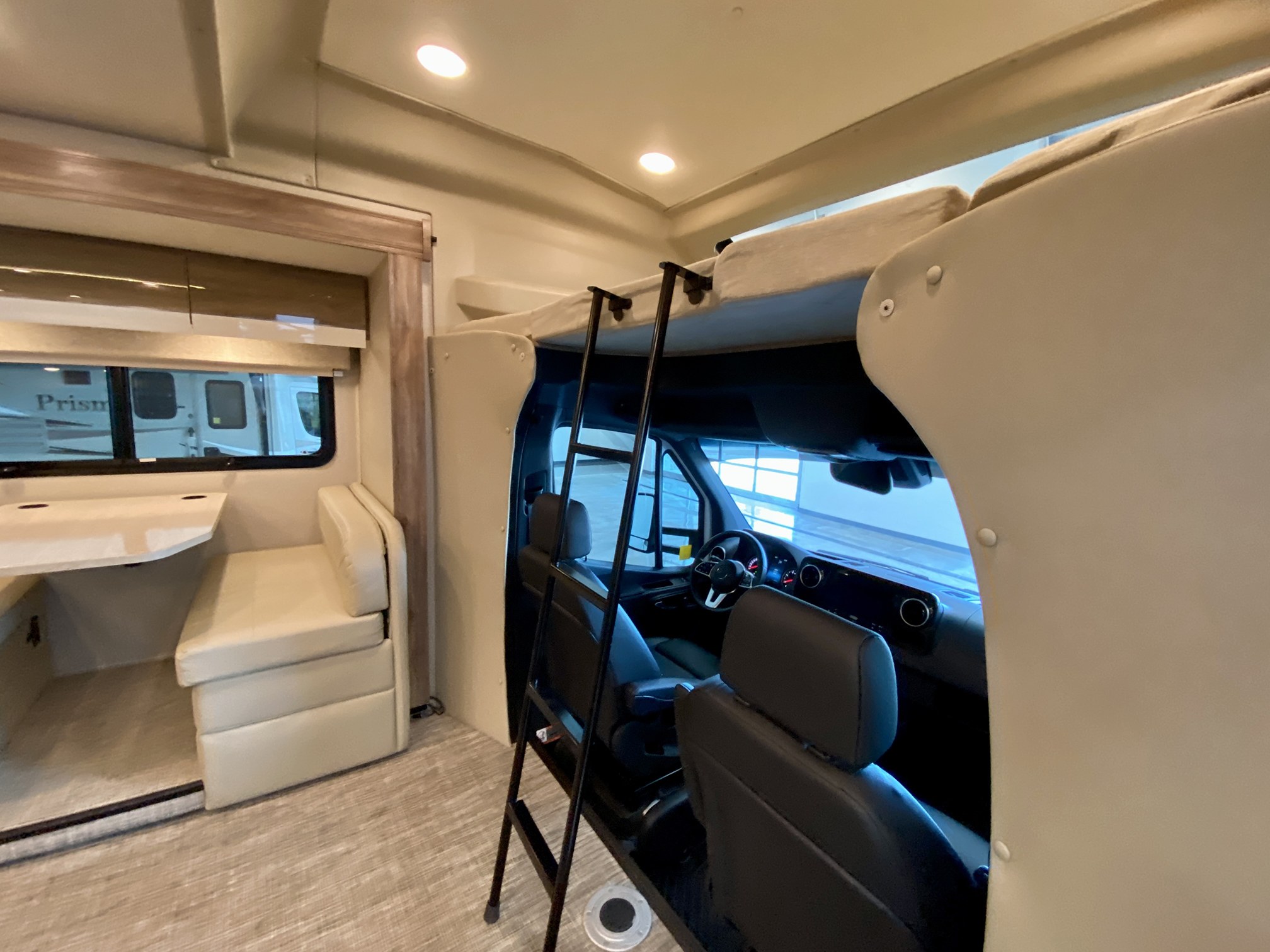 Bright rv rental interior, showing a cab-over bed with ladder, spacious front cabin, and a cozy dining area to the left.. Entegra Coach Qwest 2020