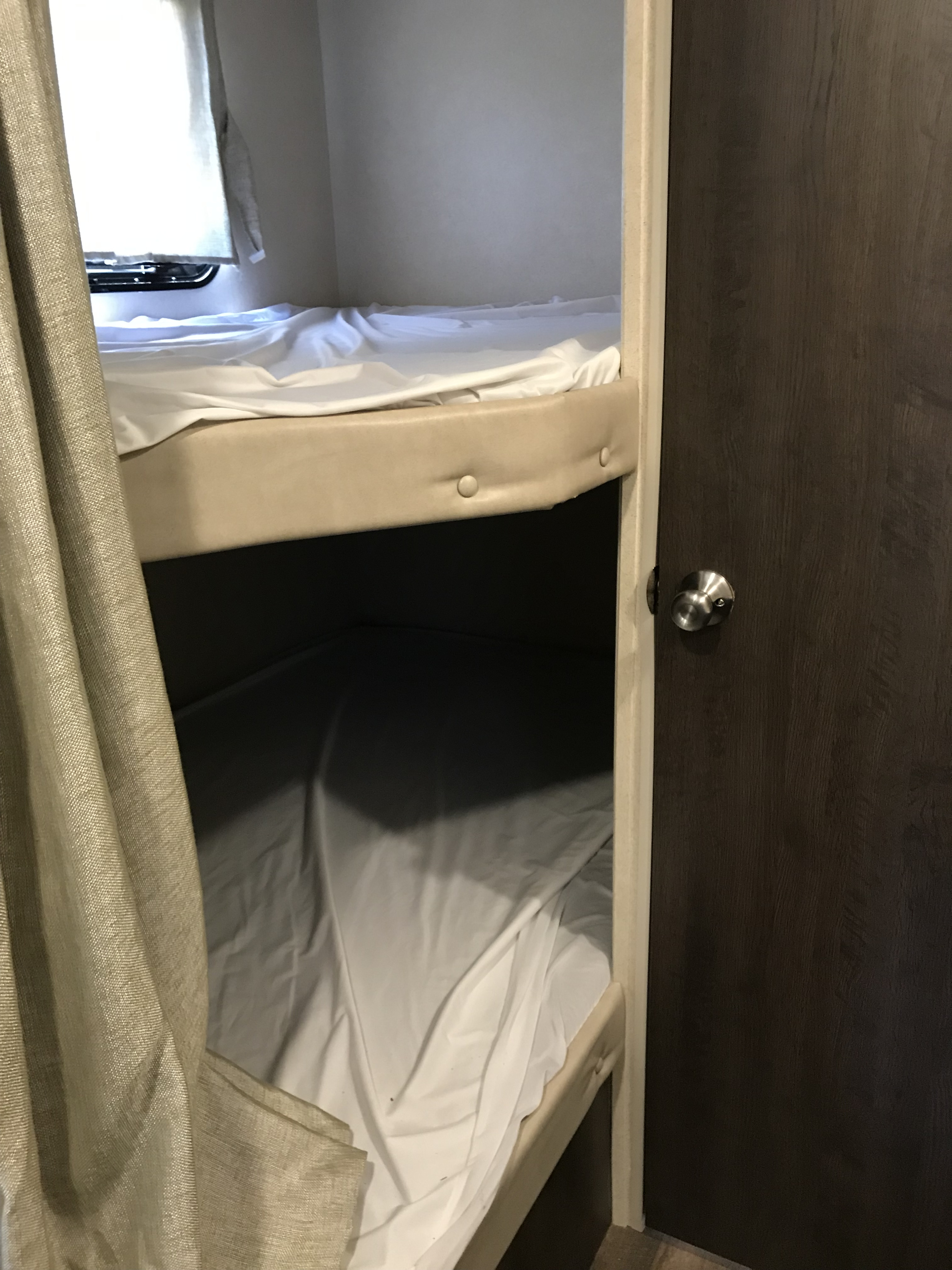 Compact and cozy RV rental interior featuring two bunk beds with white sheets, a window, and a wooden door.. Forest River Salem Cruise Lite 2018