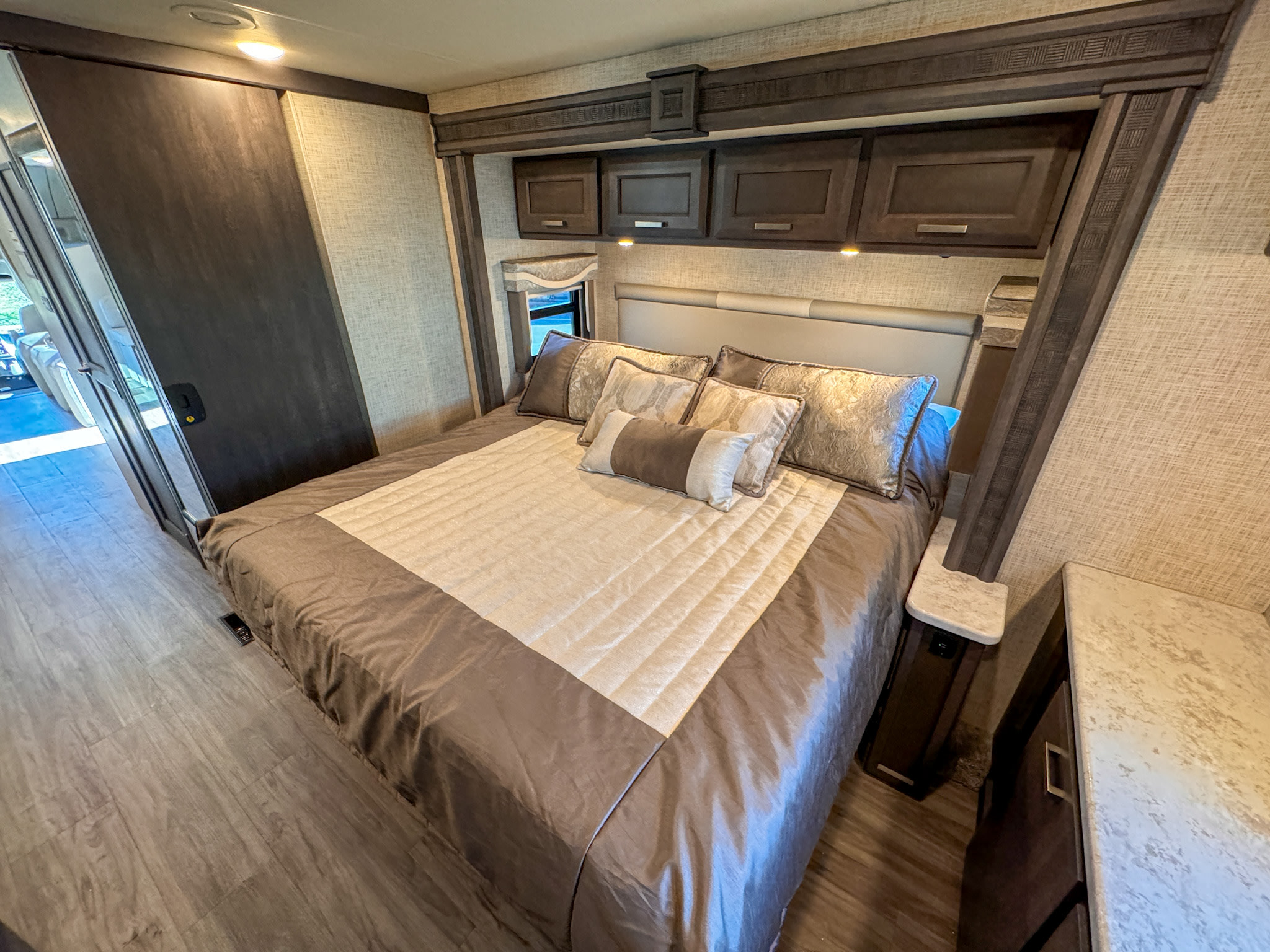 Cozy rv rental bedroom with a large bed, built-in overhead cabinets, and wood flooring. Ideal for comfortable travel.. Thor Motor Coach Pasadena Super-C 2023