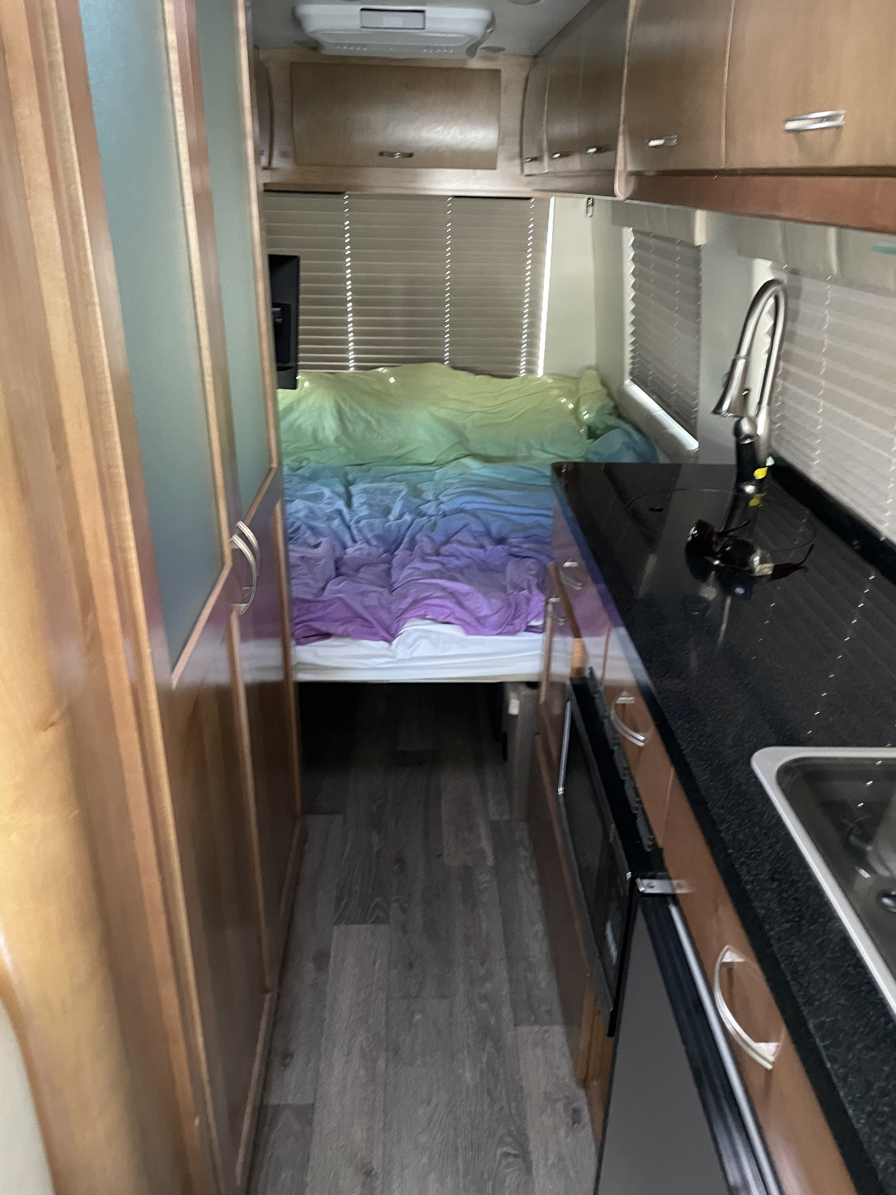 RV rental interior: narrow aisle to a bed with colorful ombre bedding, and a compact kitchenette on the right.. Mercedes Benz Sprinter 2018