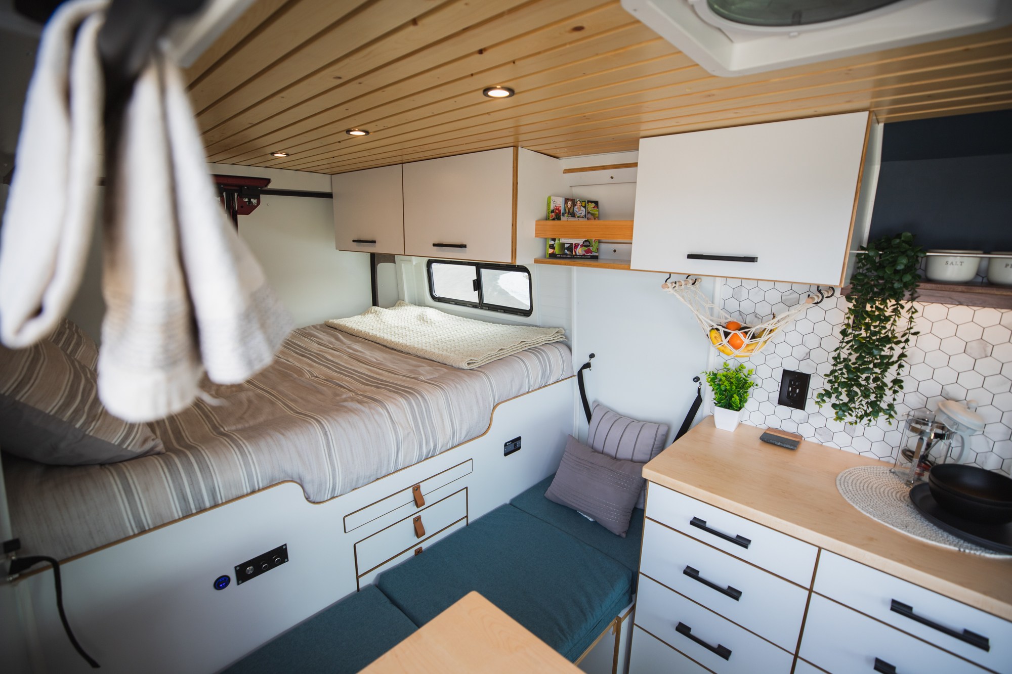 Cozy RV rental interior featuring a comfortable bed, modern kitchen with hex tiles, wood ceiling, and smart storage.. Dodge Ram ProMaster 2021