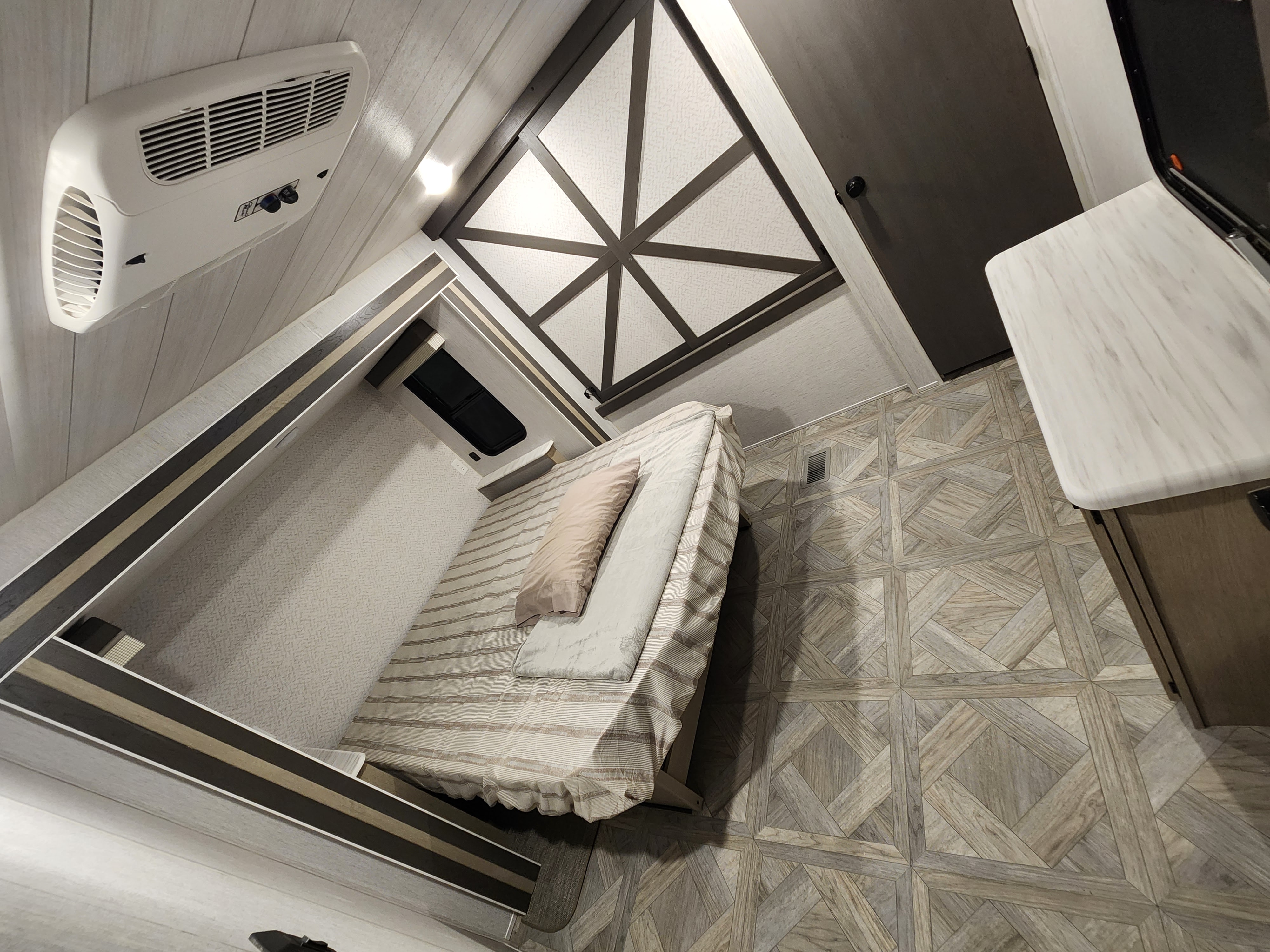 Modern RV rental bedroom: AC unit, textured ceiling, cozy bed, and patterned wood-look flooring.. Forest River Wildwood 2023
