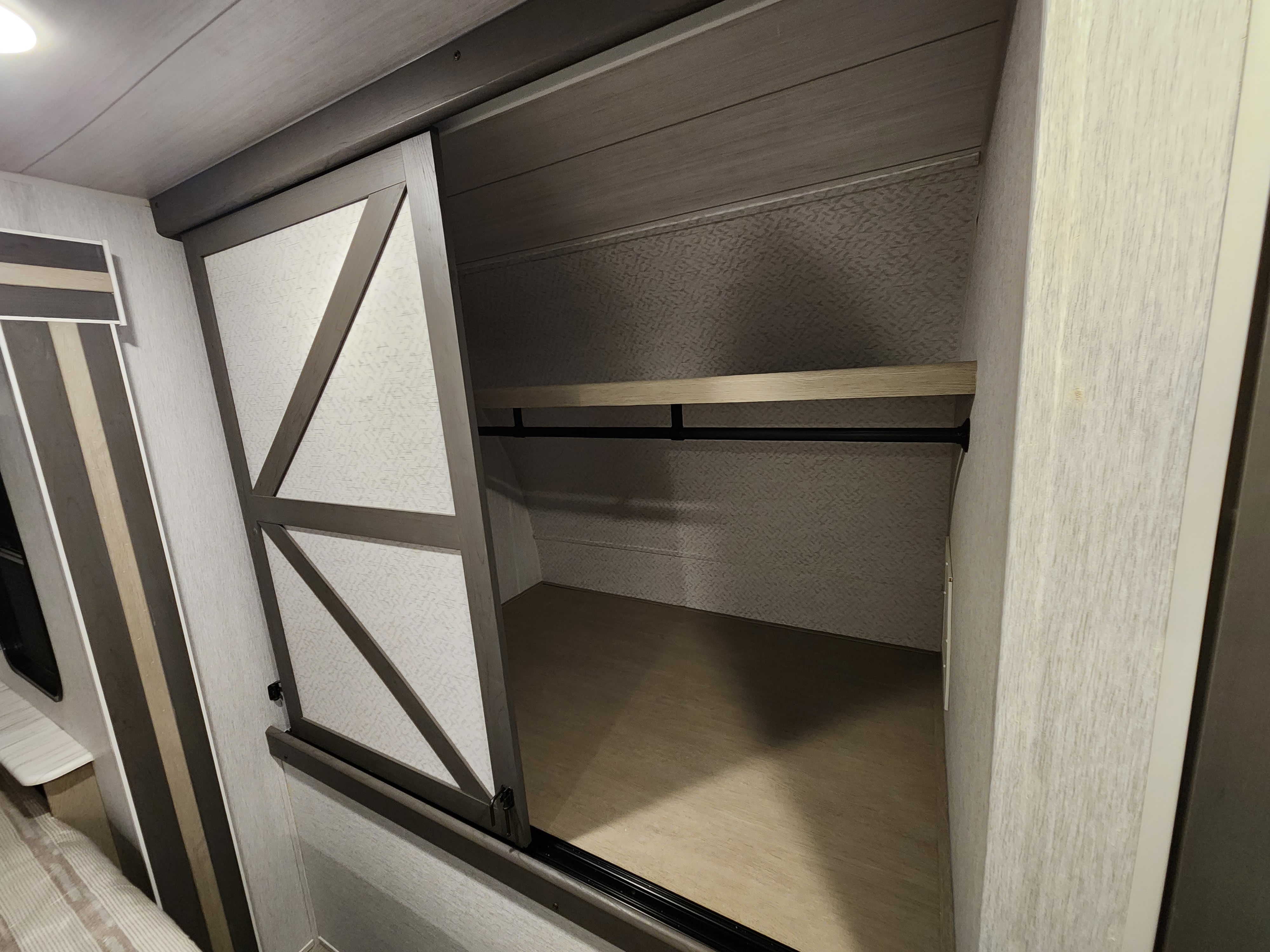 Inside an RV rental: a modern closet with a patterned sliding door, shelf, and hanging rod for storage.. Forest River Wildwood 2023