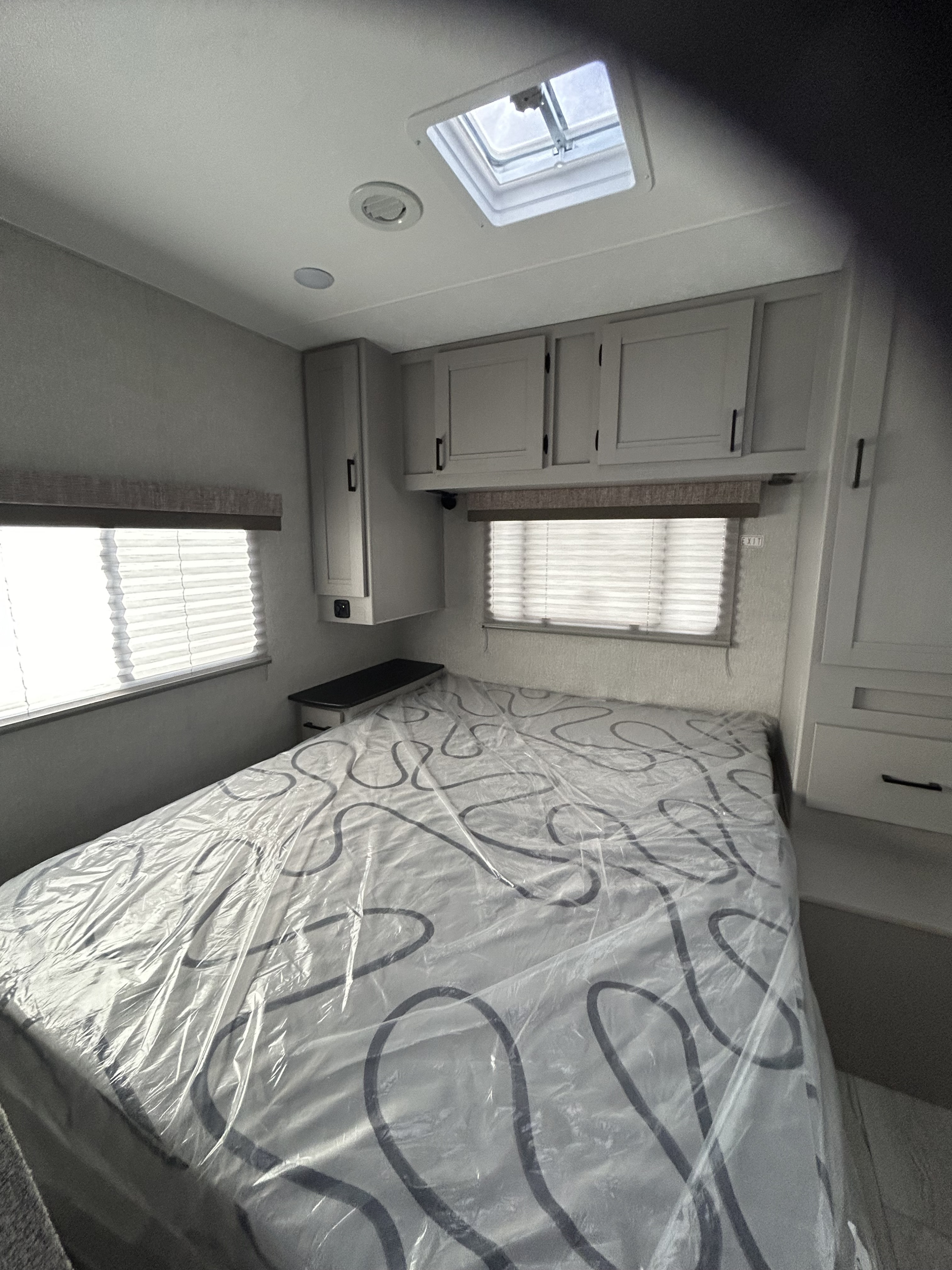 RV rental bedroom interior with plastic-covered mattress, light gray cabinets, windows, and skylight overhead.. Forest River Freelander 2024