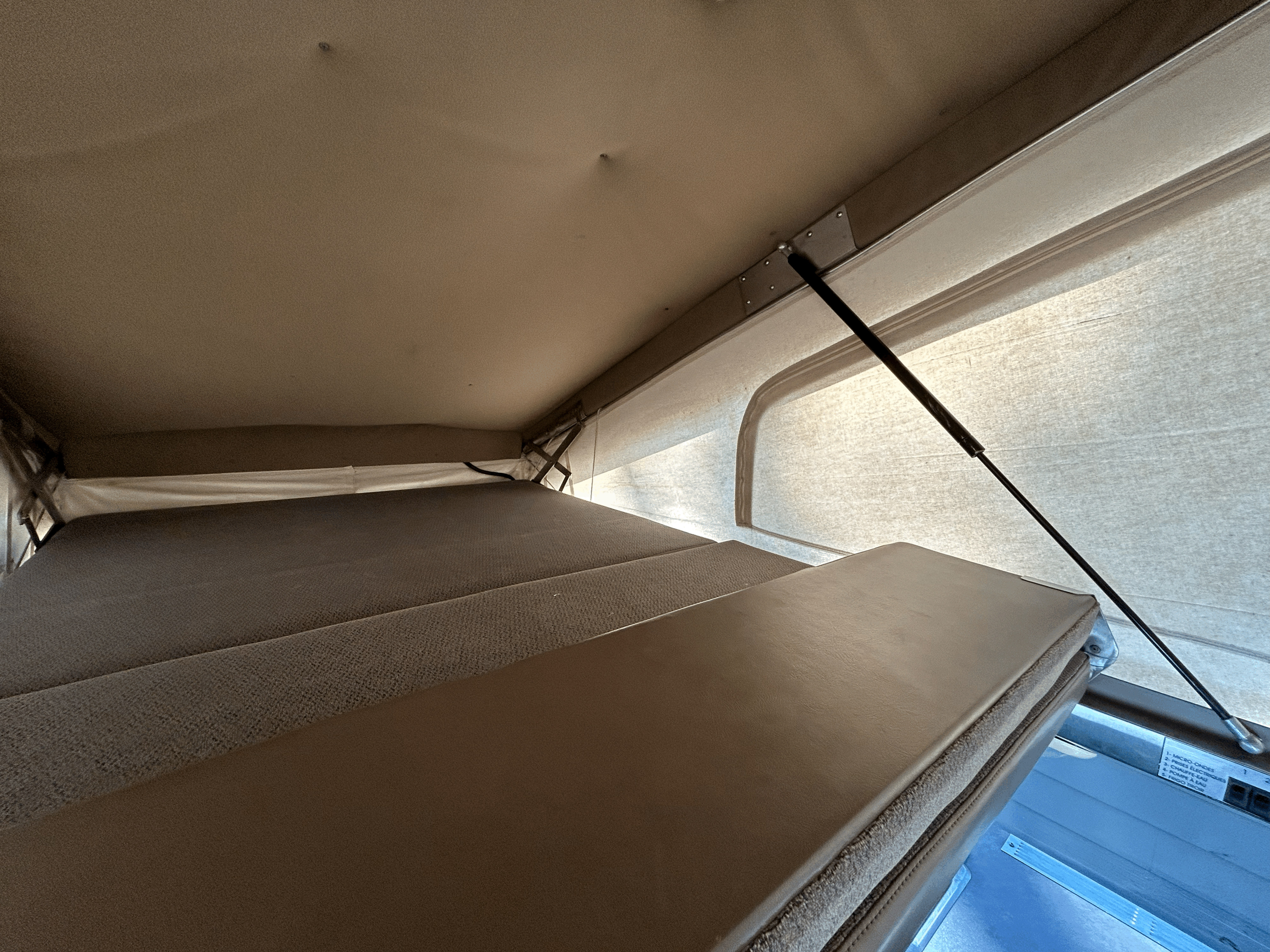 Inside an RV rental: a cozy pop-top camper bed setup with fabric walls and a control panel for amenities like microwave & water.. Chevrolet Astro 1997