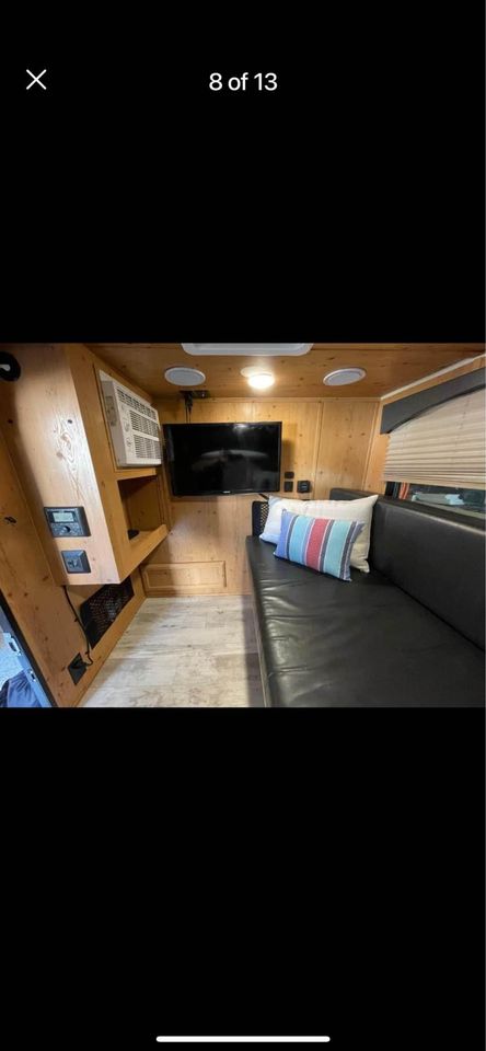 Spacious RV rental interior: wood-paneled walls, black sofa with pillows, mounted TV, and AC unit.. Sunset Park RV SunRay 2020
