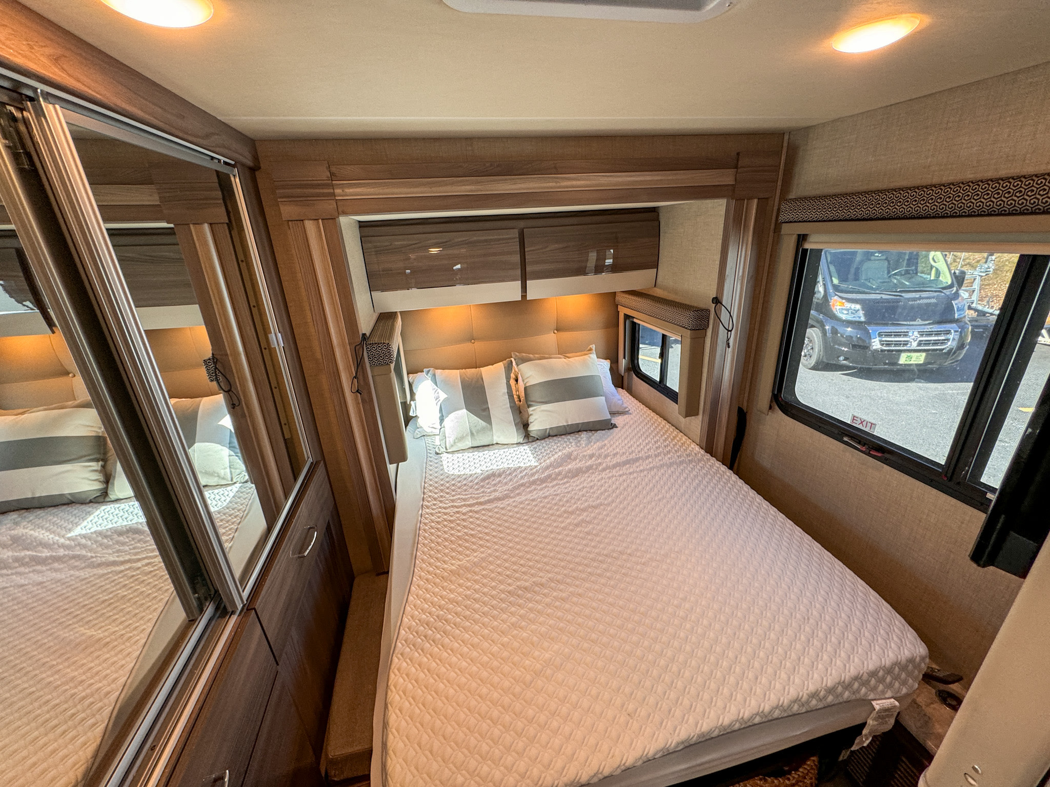 Cozy rv rental bedroom interior with a comfortable bed, mirrored closet, and window view, perfect for travel.. Thor Motor Coach Delano 2022