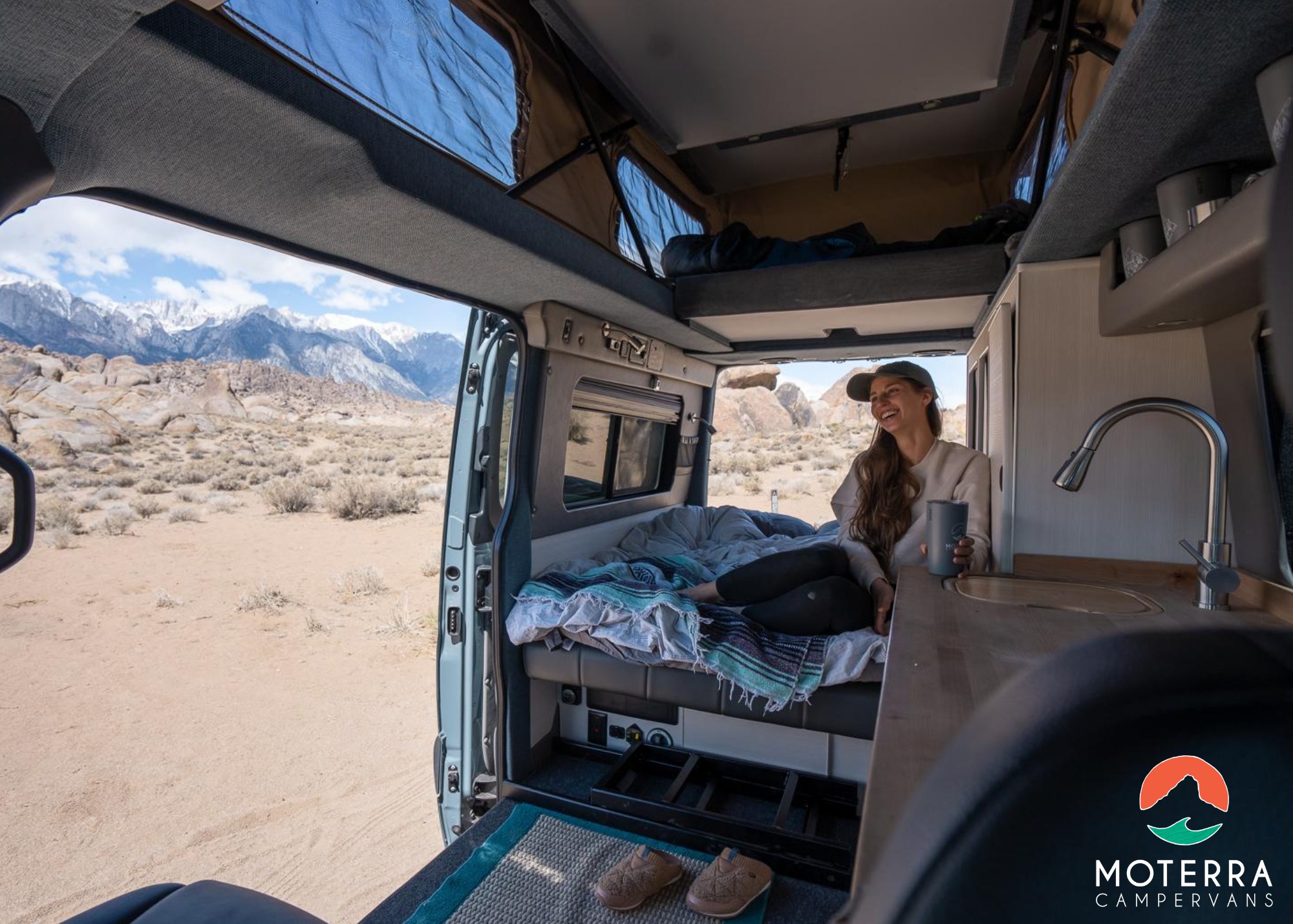 Inside a cozy RV rental camper van, a woman enjoys stunning desert and snowy mountain views through the open doors. Perfect for adventures.. Mercedes-Benz Sprinter 2020