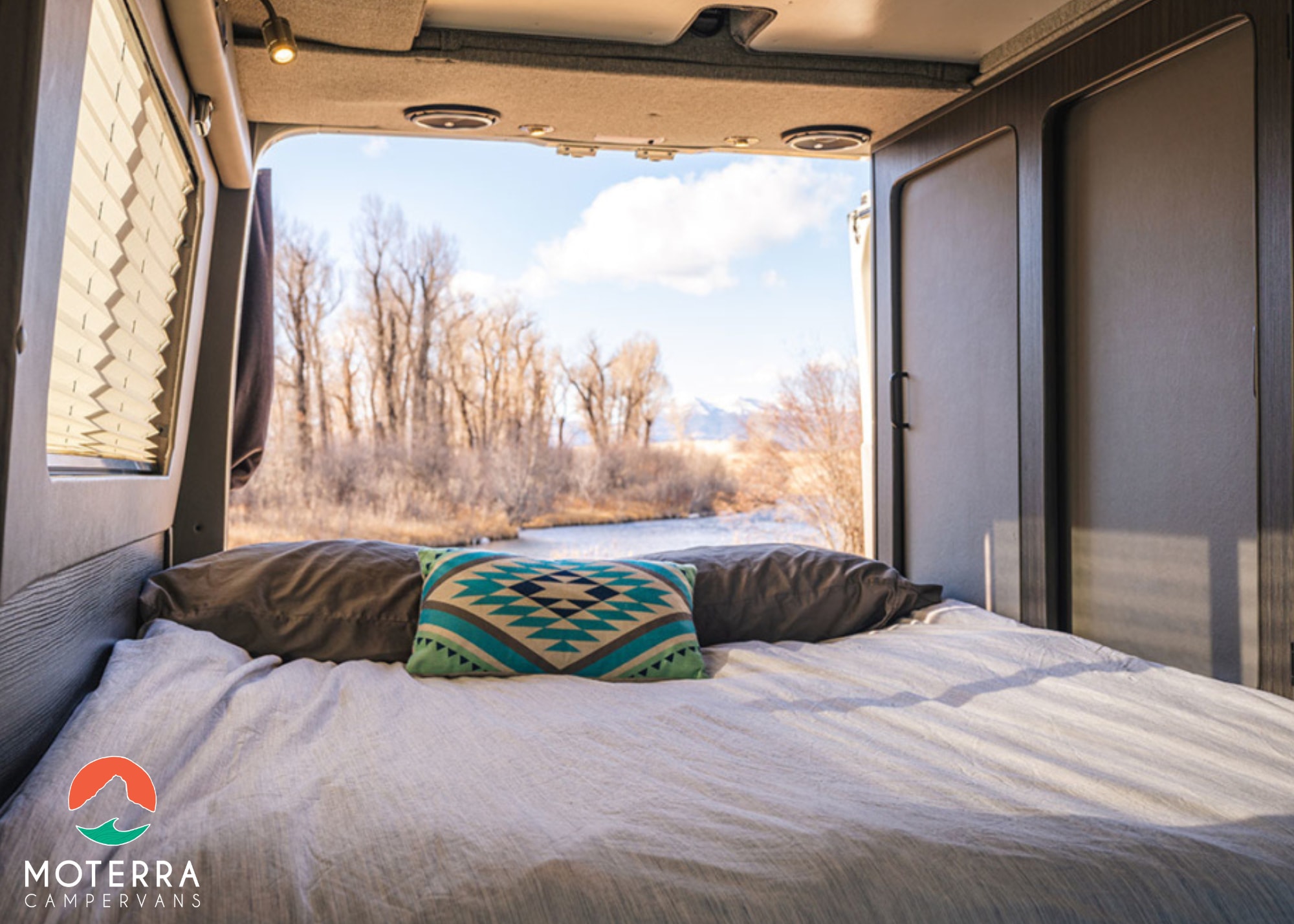 Cozy RV rental bed with open doors revealing a scenic river, trees, and mountains. Perfect camper van escape!. Mercedes-Benz Sprinter 2020