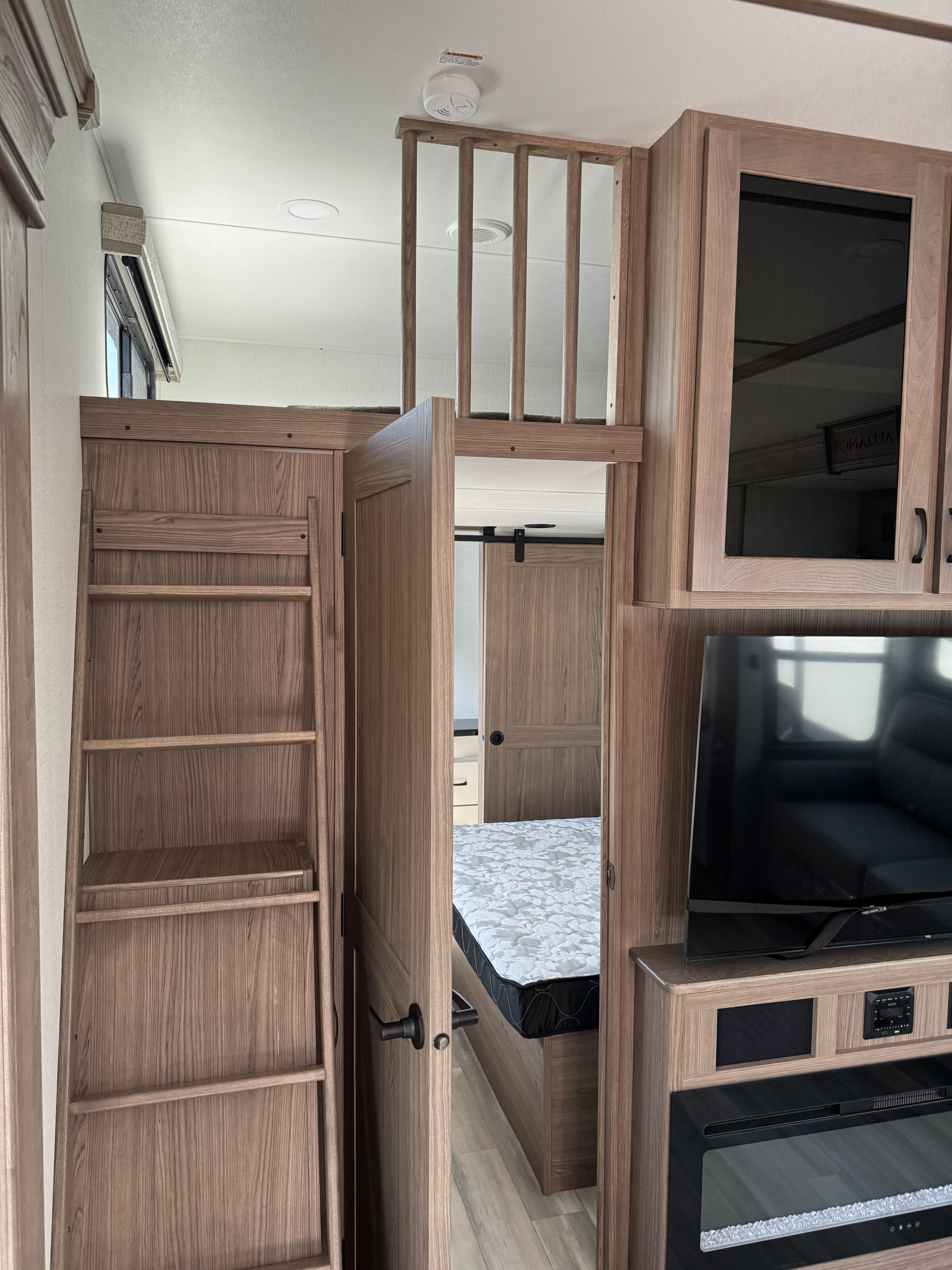 RV rental interior: cozy bunk bed area with ladder, glimpse of a bedroom, and a built-in TV with fireplace.. Alliance RV Paradigm 2023