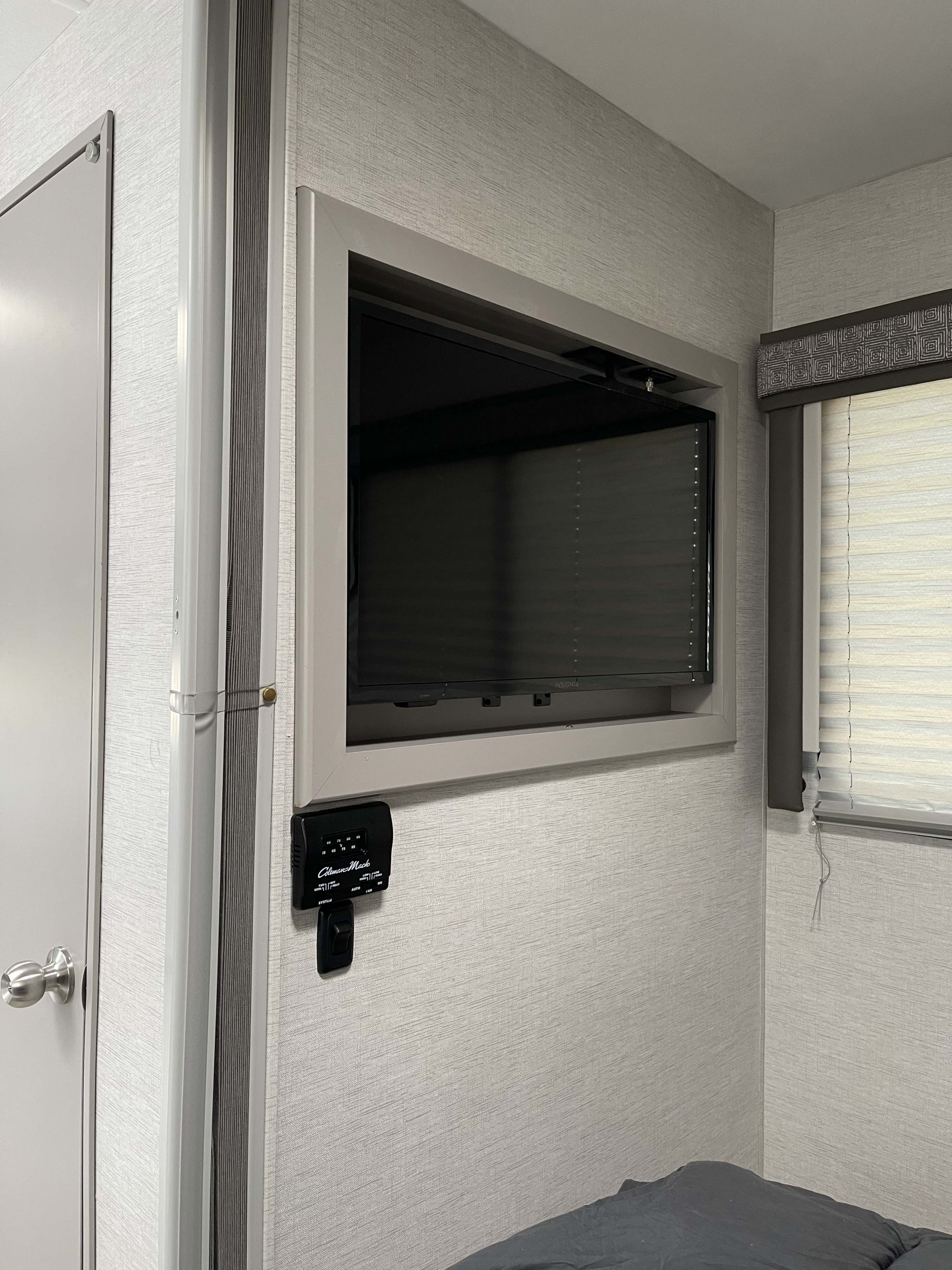 RV rental bedroom featuring a wall-mounted TV, Coleman-Mach thermostat, and window blinds for comfort.. Thor Motor Coach Chateau 2024