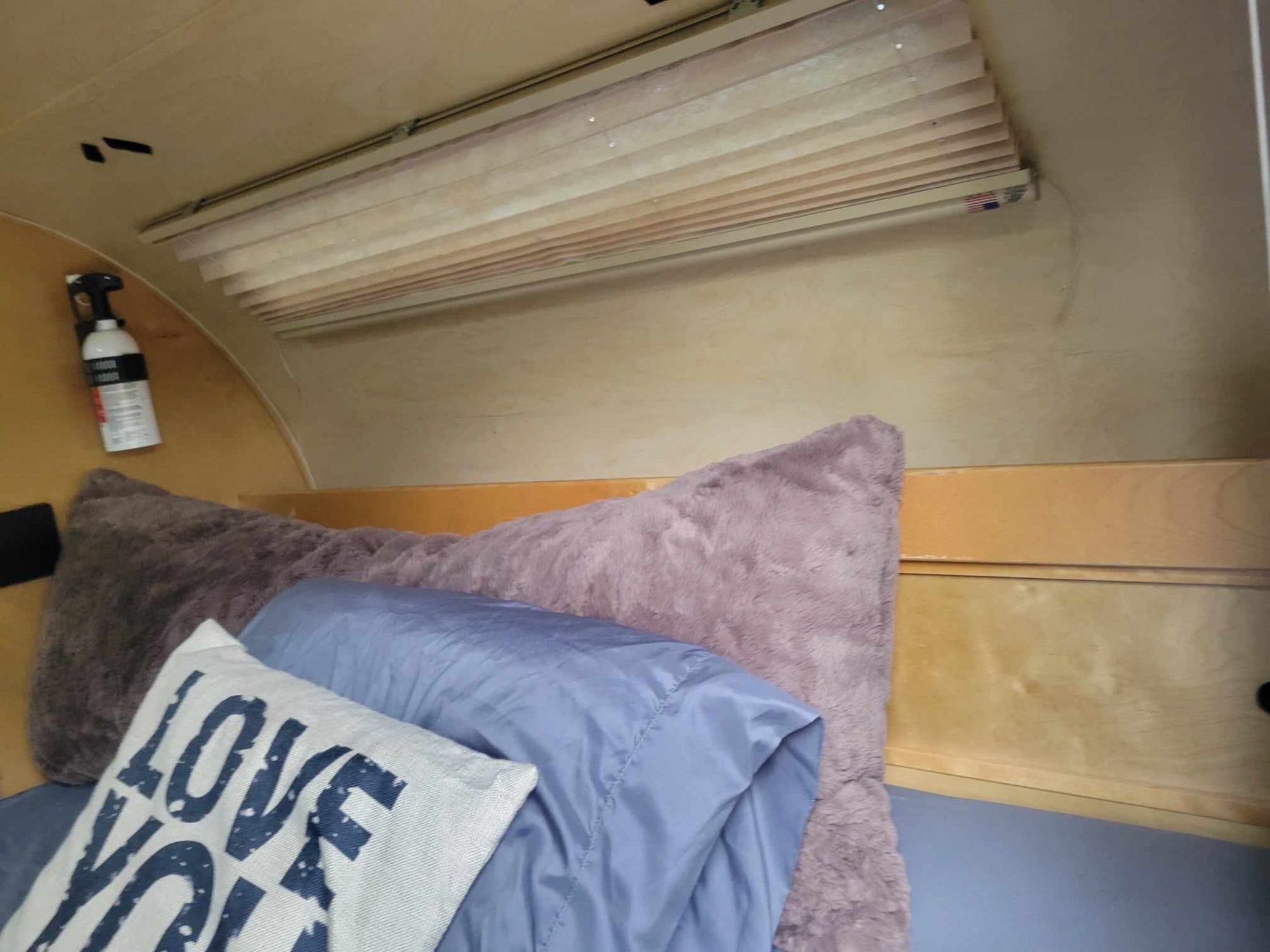 Cozy RV rental interior: A bed with soft pillows, light-colored pleated blinds, and a fire extinguisher.. Little Guy Silver Shadow 5x10 2015