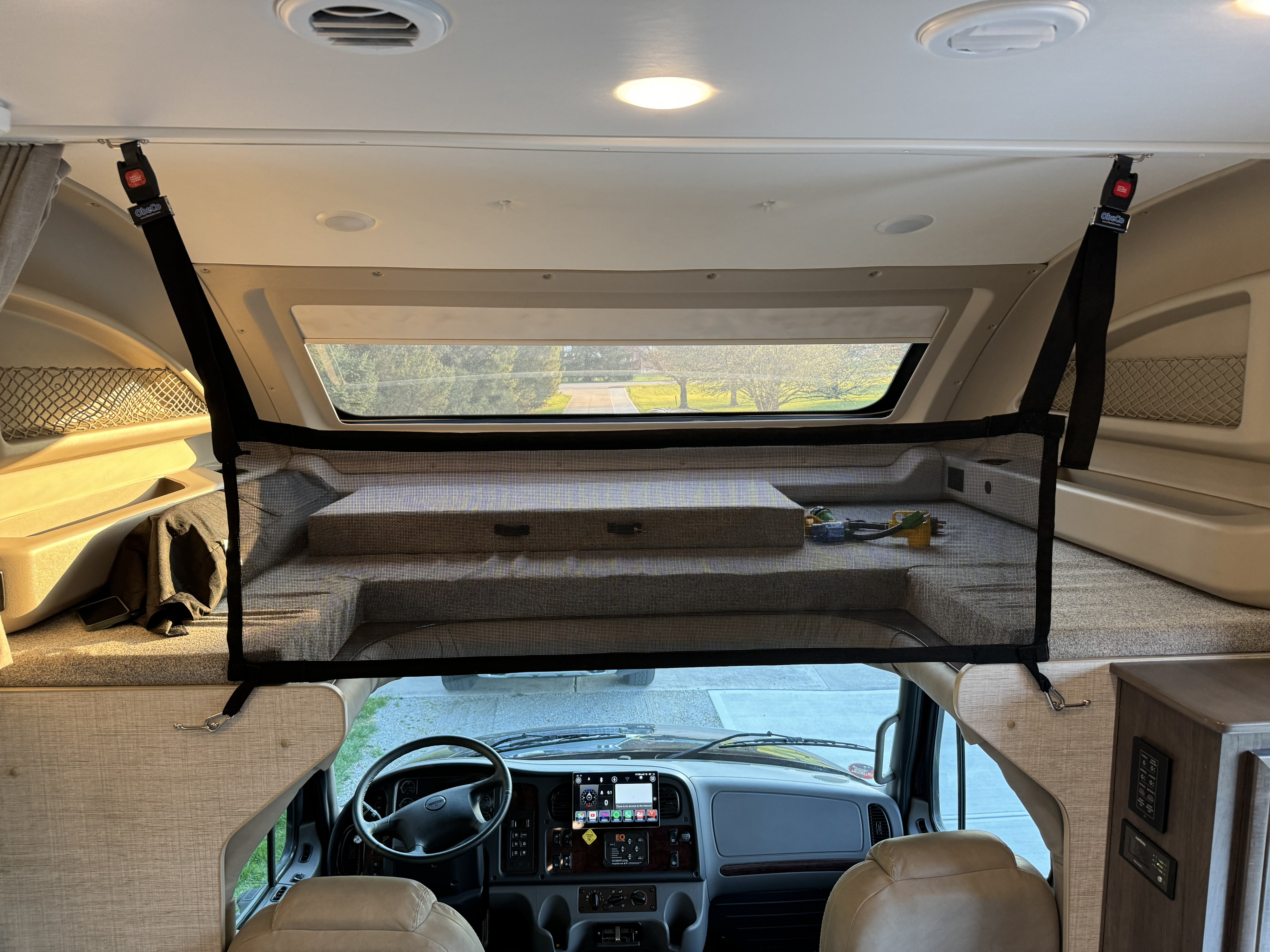 Inside an RV rental: A spacious cab-over bunk with a black mesh safety net above the driver's dashboard.. Jayco Redhawk 2022