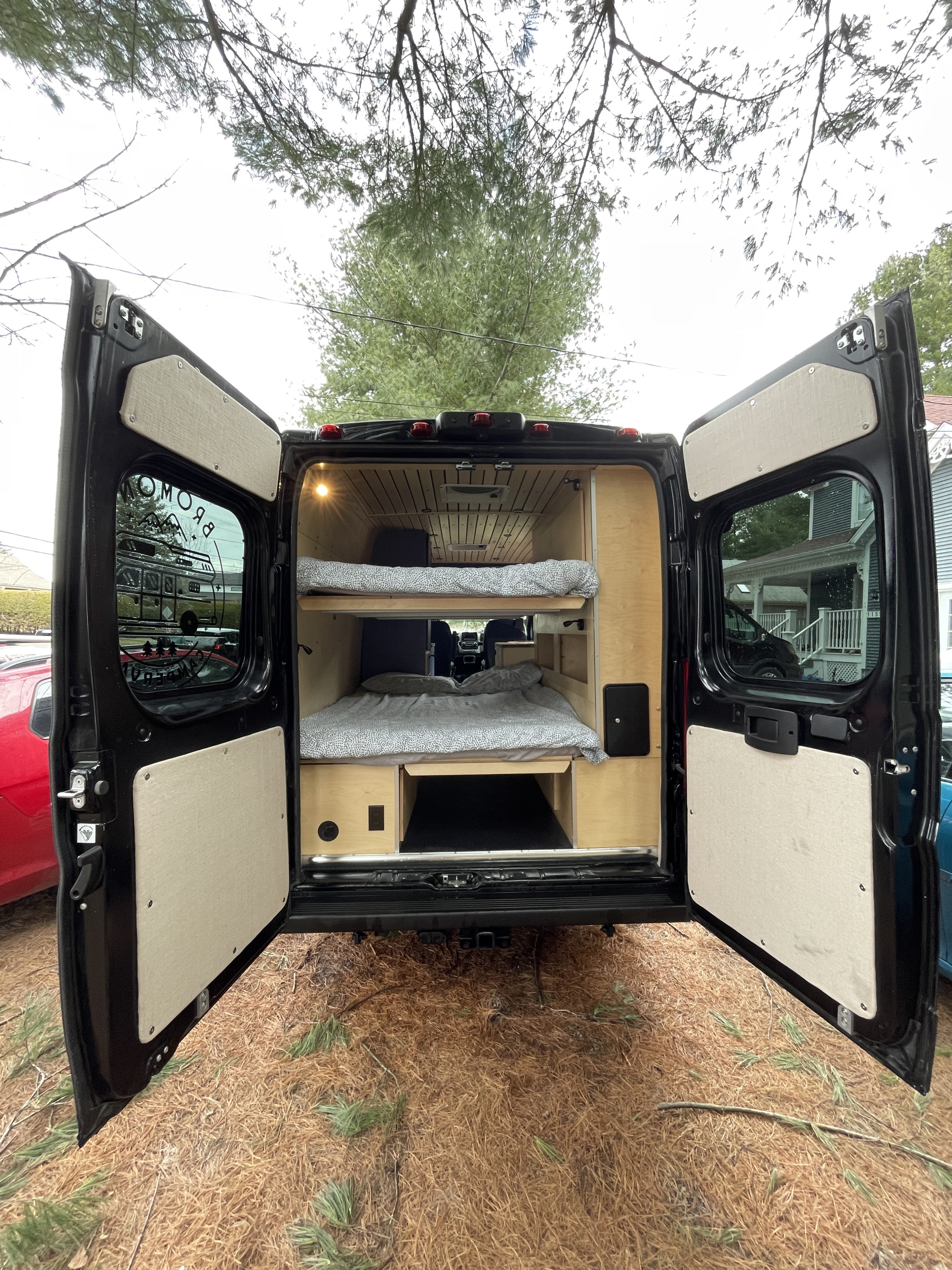 Discover this spacious RV rental! Rear view of a black camper van with open doors, showcasing custom wood bunk beds & storage.. Dodge Sportsman 2022