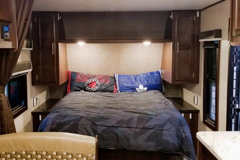 Cozy RV rental bedroom featuring a comfortable bed, overhead cabinets, and sports team pillows.. Jayco Jay Flight SLX Baja Edition 2019