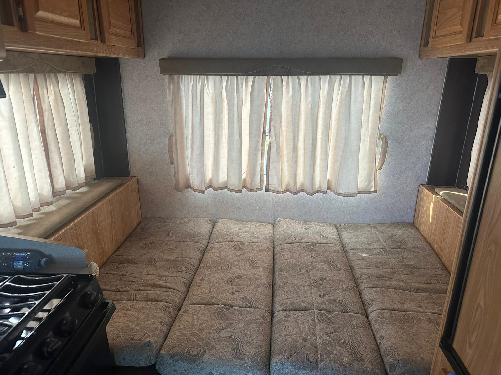 RV rental interior featuring a compact living space with a bed, multiple windows with curtains, and a kitchen area.. Adventurer Adventurer Motorhome 2007