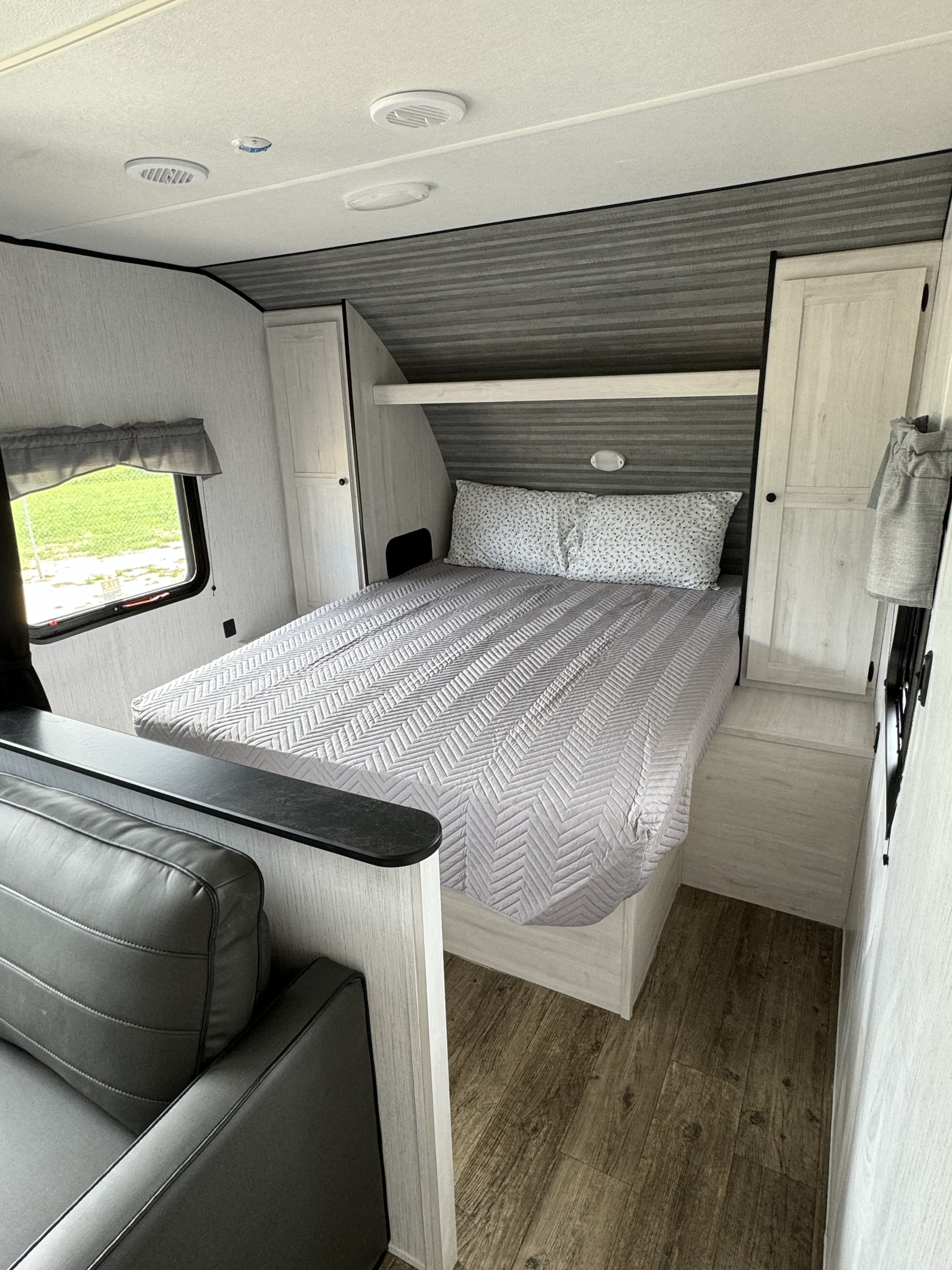 Cozy RV rental bedroom with a comfy bed, overhead storage, and partial view of living area.. Heartland RVs Trail Runner 2023