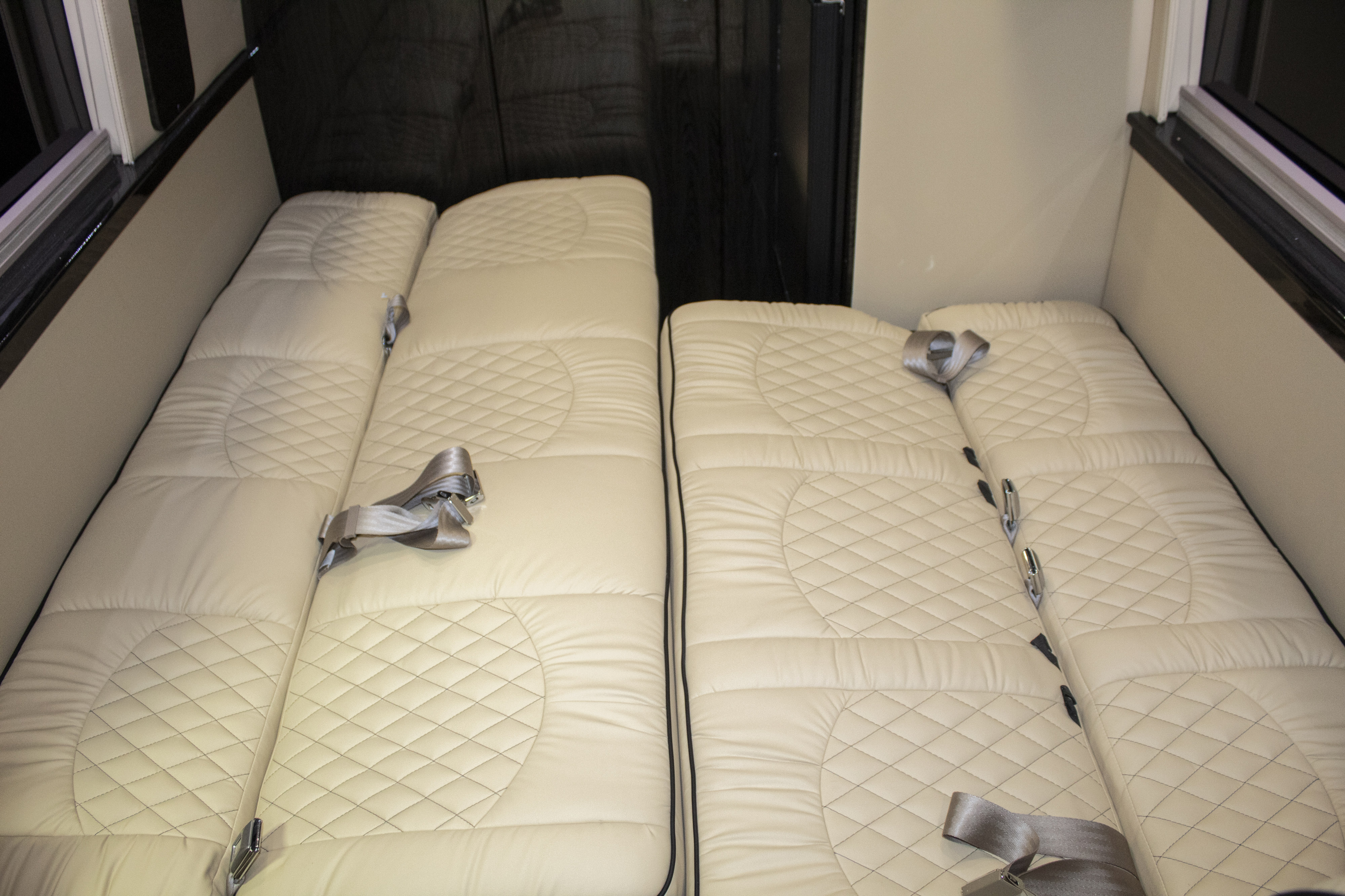 RV rental interior: Two plush, cream-colored quilted benches/beds with seatbelts, ideal for travel comfort.. Ultimate Toys Ultimate RV 2024