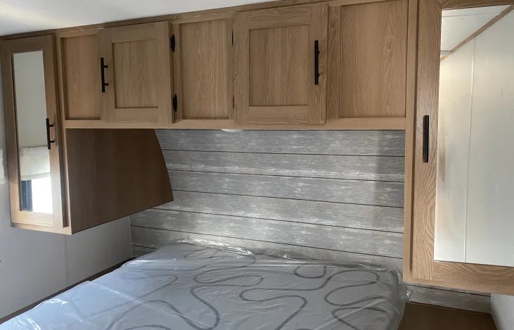 Cozy RV rental bedroom with light wood cabinets, headboard, and bed. Perfect for your next adventure.. Prime Time Avenger by Forest River 26bk 2023